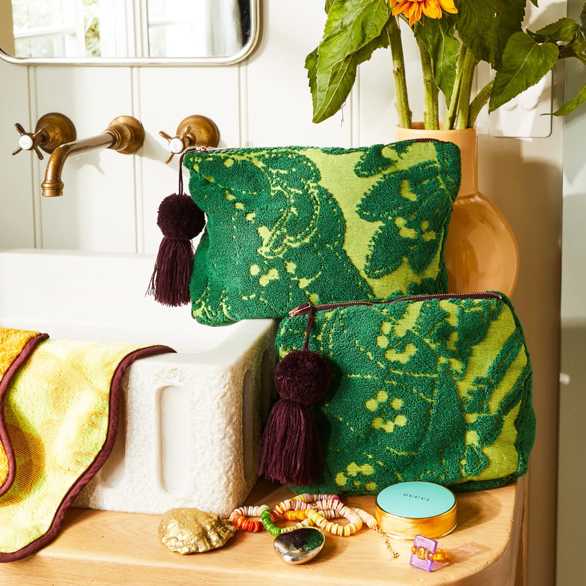 Two different sized green, printed pouches with a brown tassel on the zippers. 