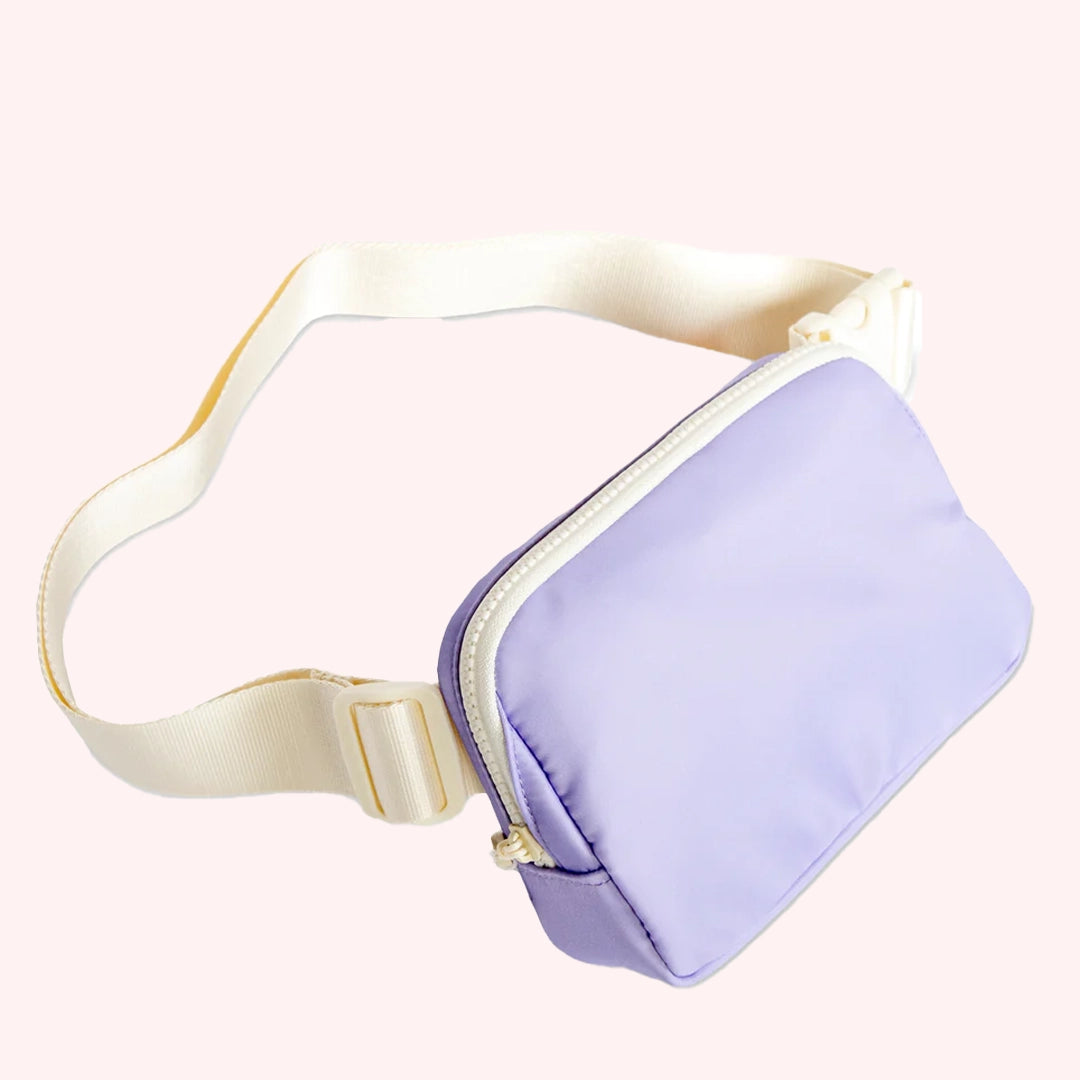 On a pink background is a lavender colored fanny pack with a cream strap. 