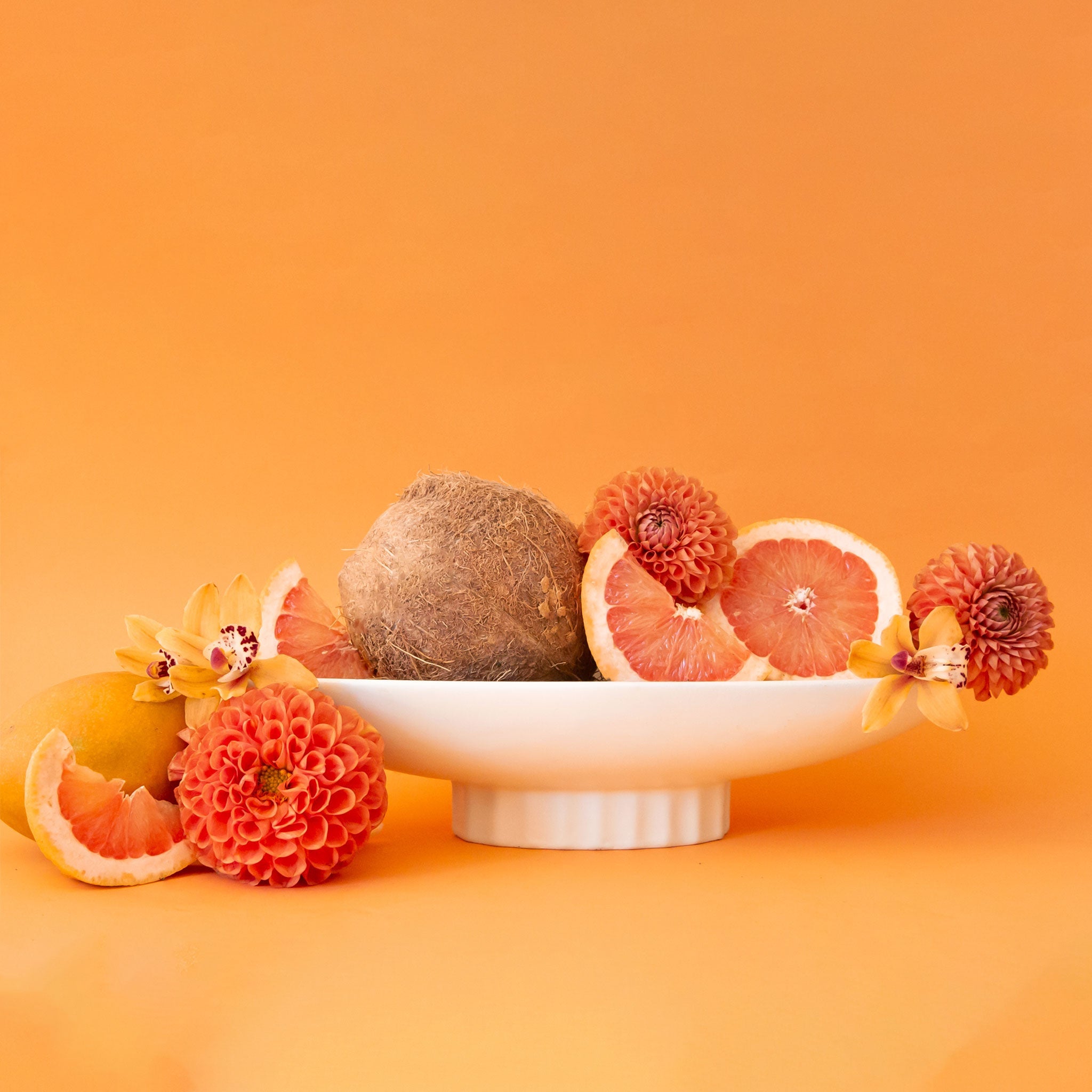 Fruit and flowers on a white planter against an orange background