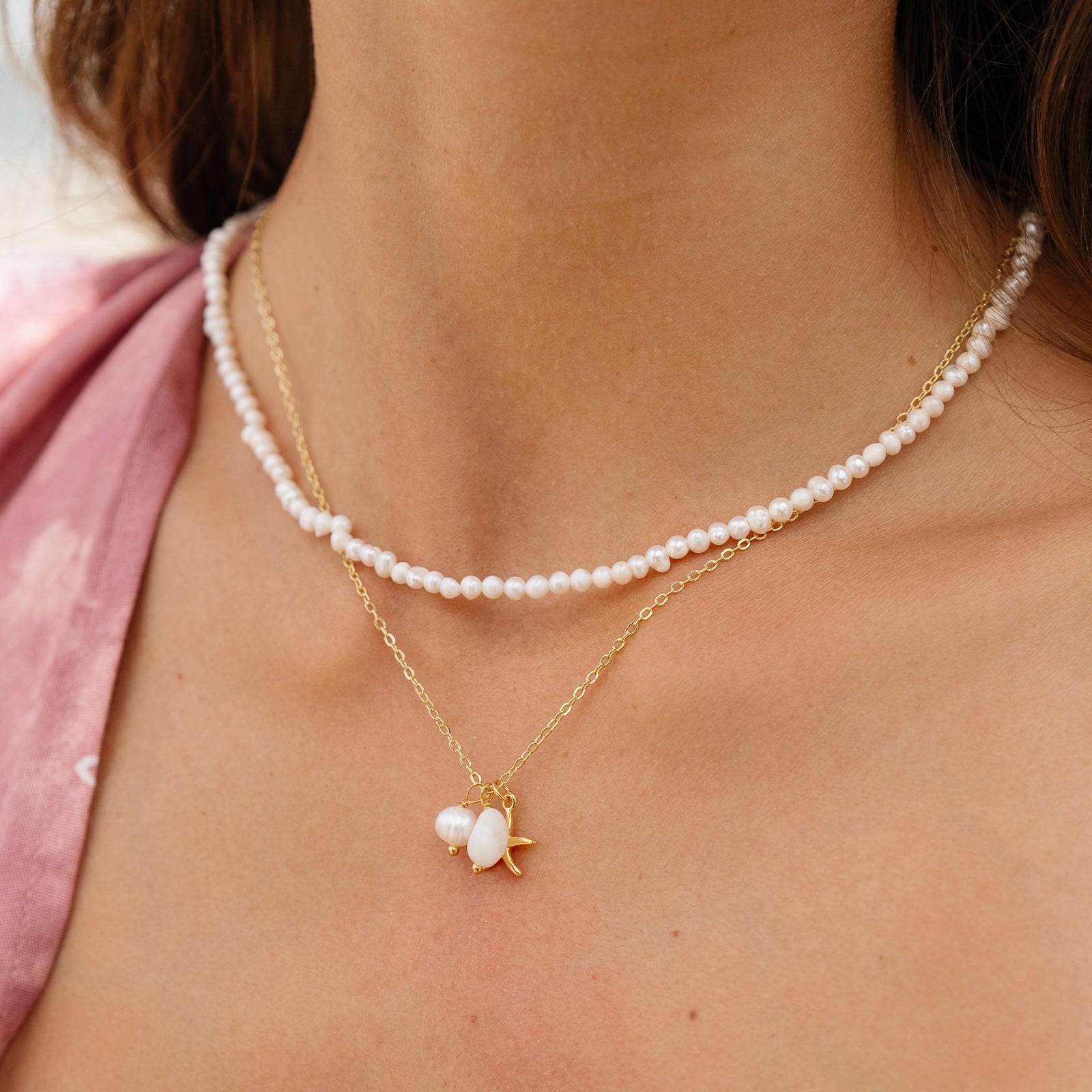 A gold chain necklace with a pearl and gold starfish pendant charm. 