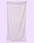 On a purple background is a light purple towel with a subtle floral print and fringe edge. 