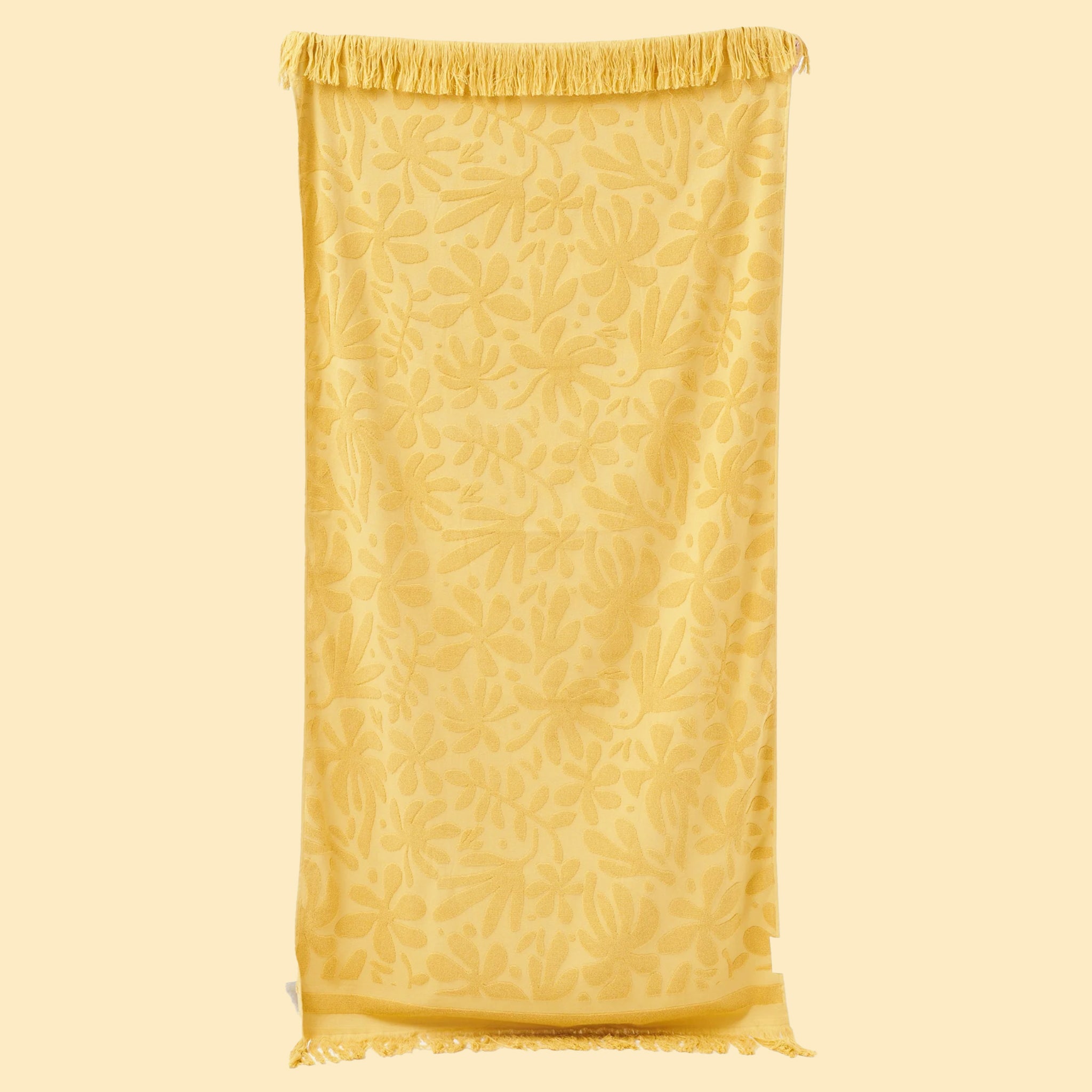 A yellow beach towel with a subtle yellow floral print and fringe edges.