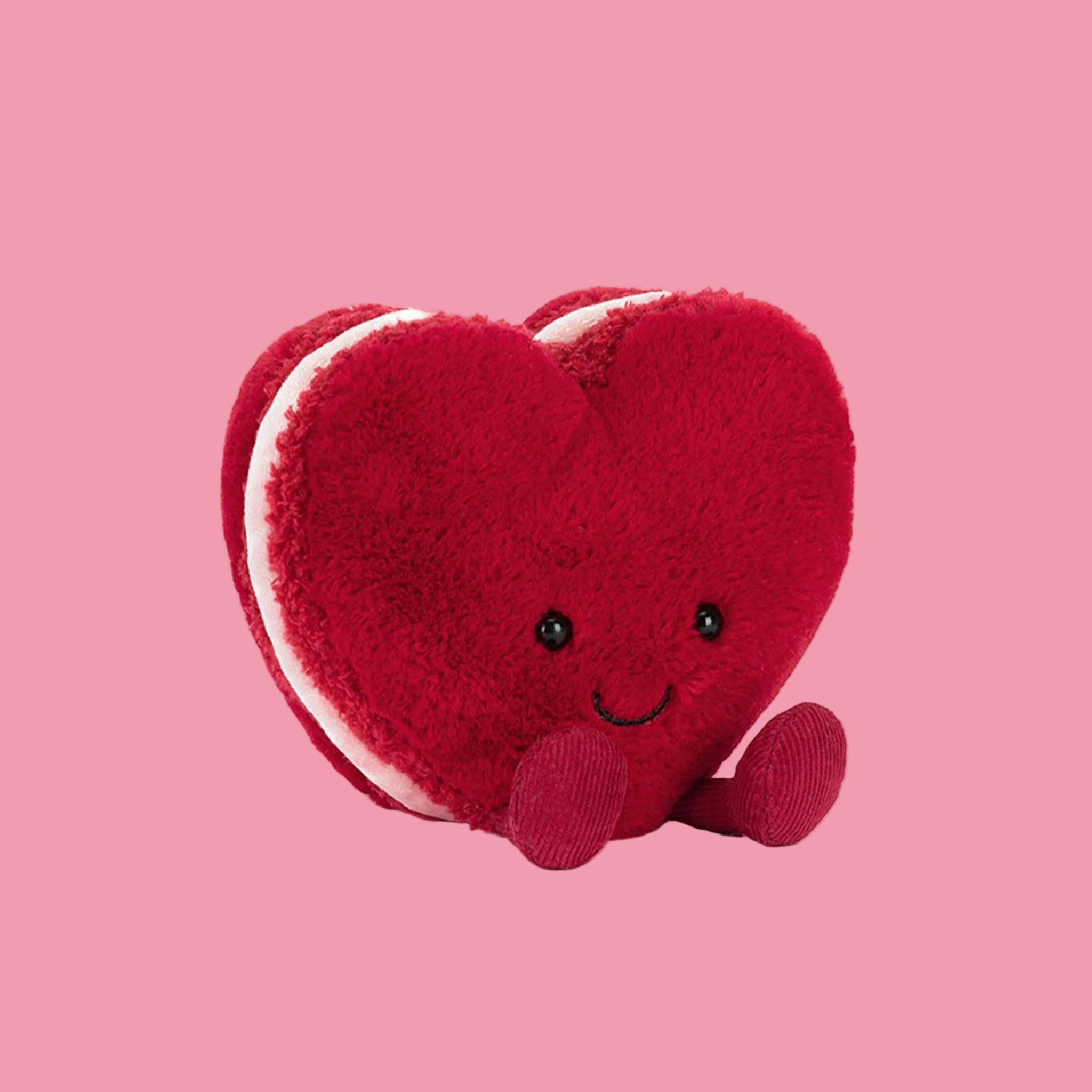 A heart shaped macaron stuffed toy with a smiling face. 
