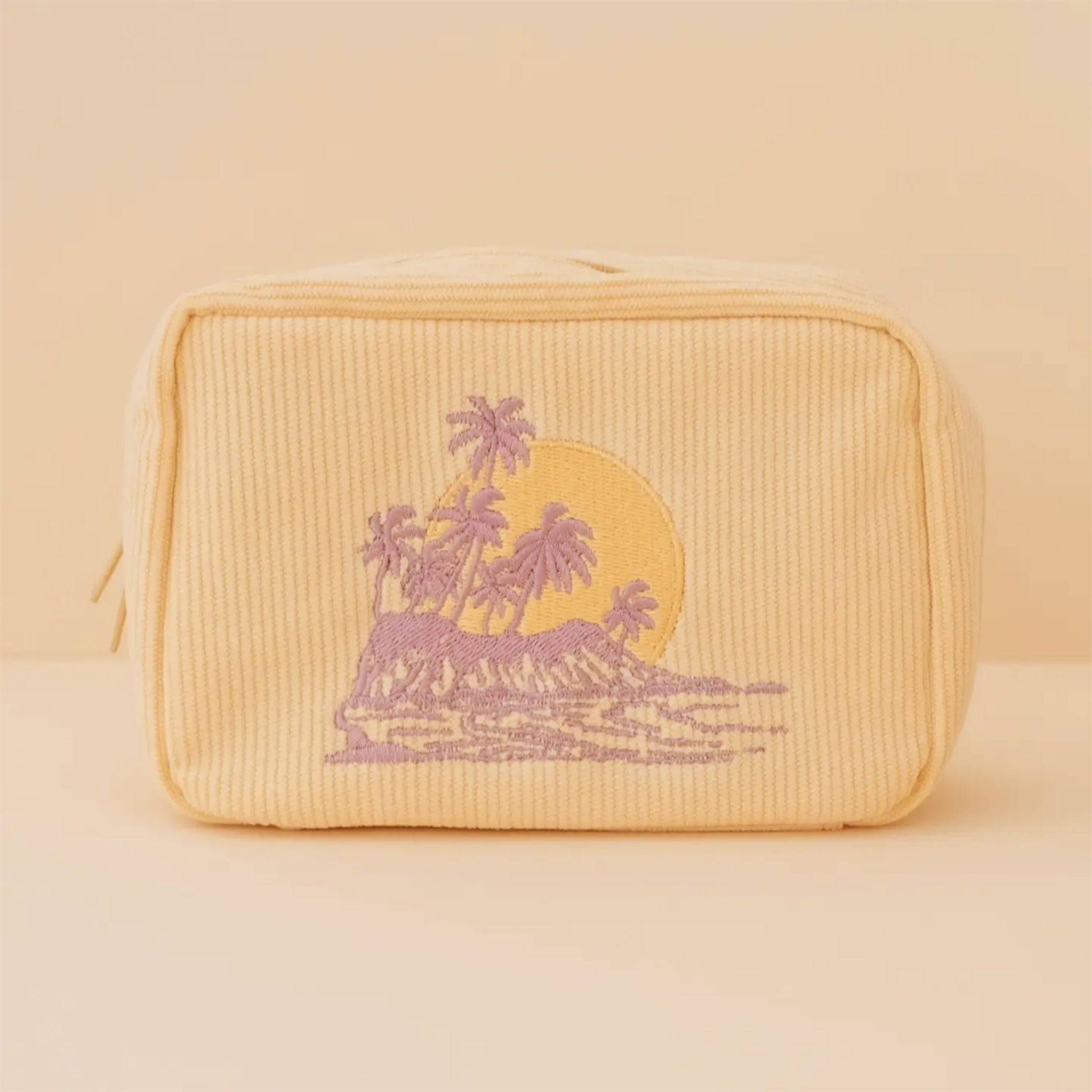 A yellow corduroy makeup bag with a purple palm tree design. 