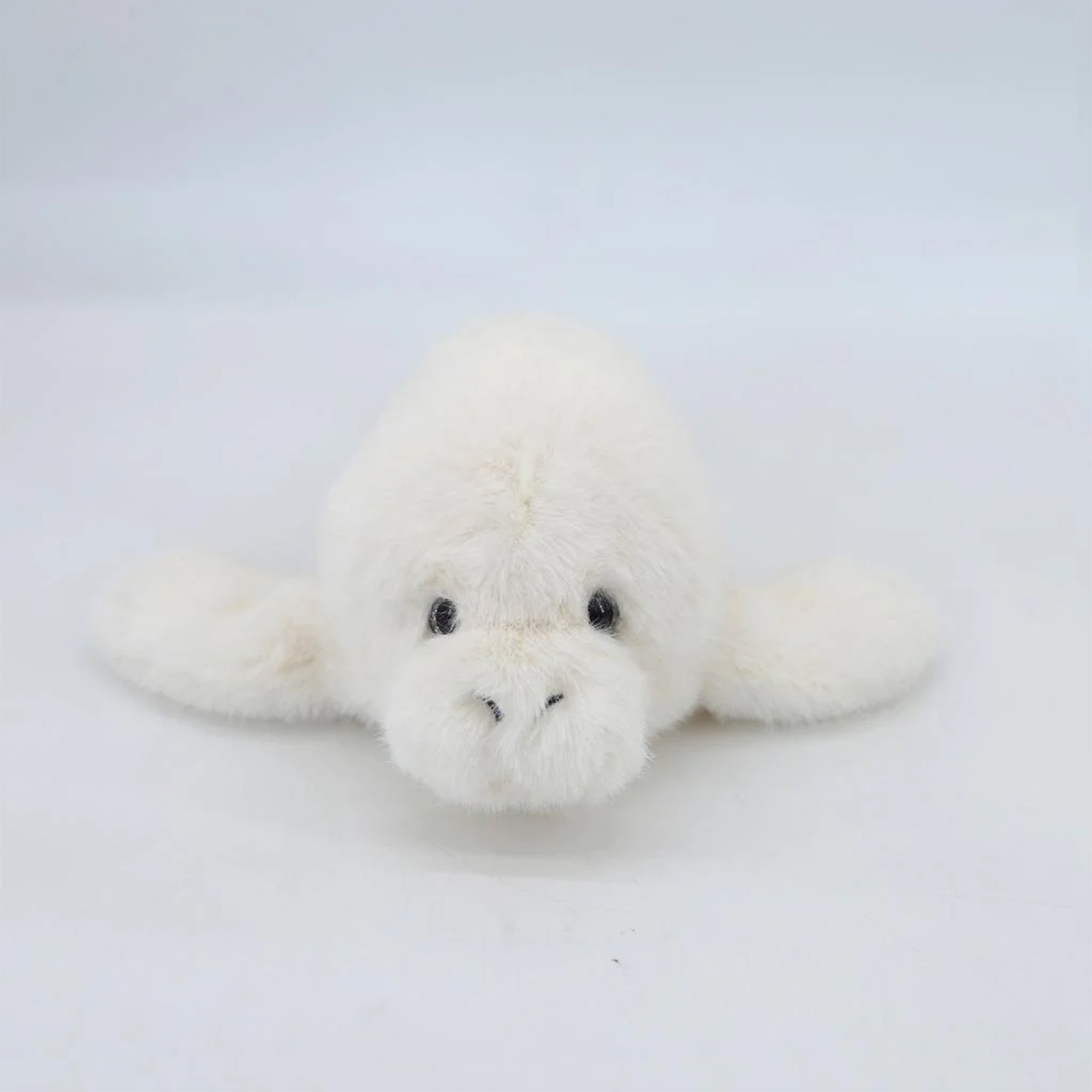 A white fuzzy manatee shaped stuffed animal toy. 