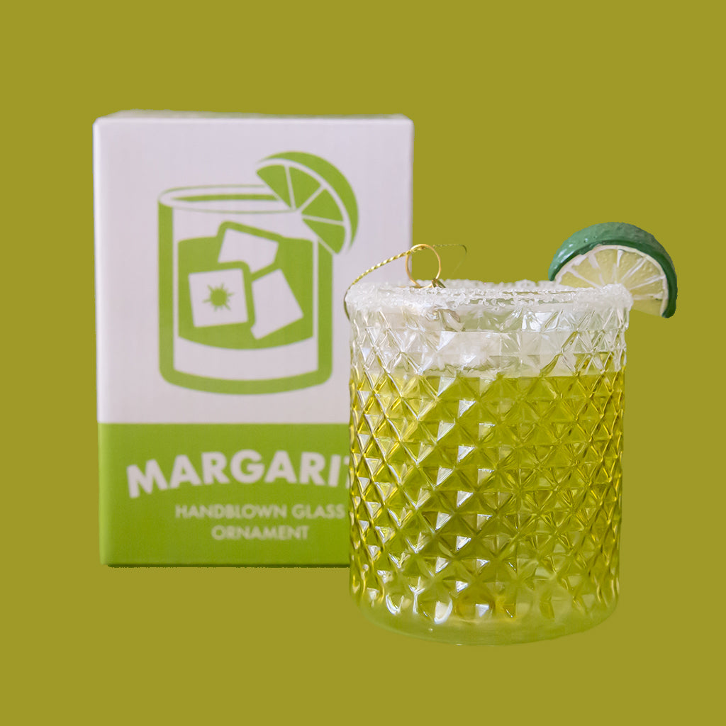 Decorative glass ornament with lime garnish next to a box labeled 'Margarita' on a green background