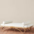 A rattan daybed with a white cushion and two pillow cushions on each end. 