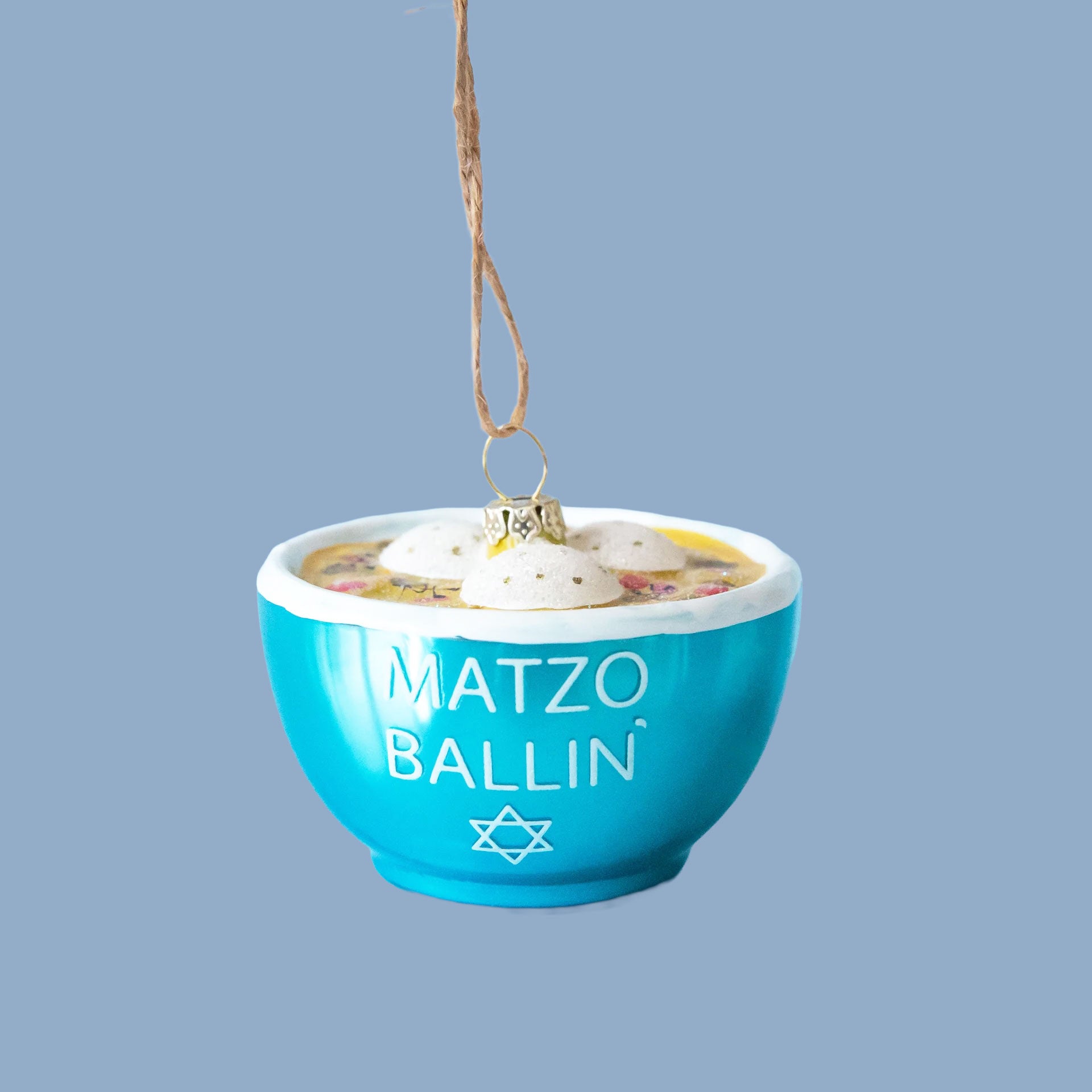 A glass matzo ball soup ornament with dumplings and a blue bowl that says "matzo ballin" in white text.