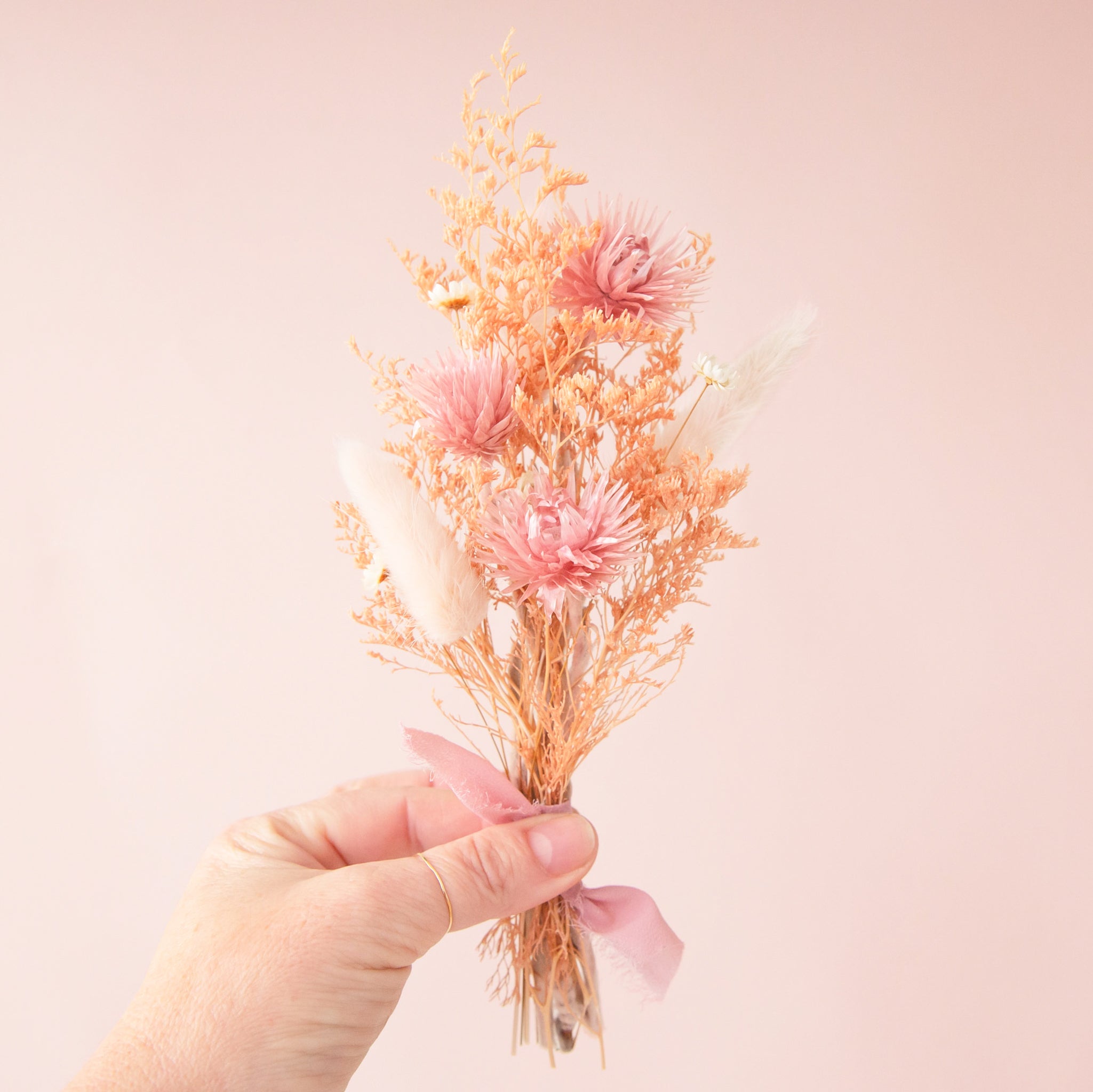A bouquet of dried florals with tan and pink flowers tied with a pink bow. 