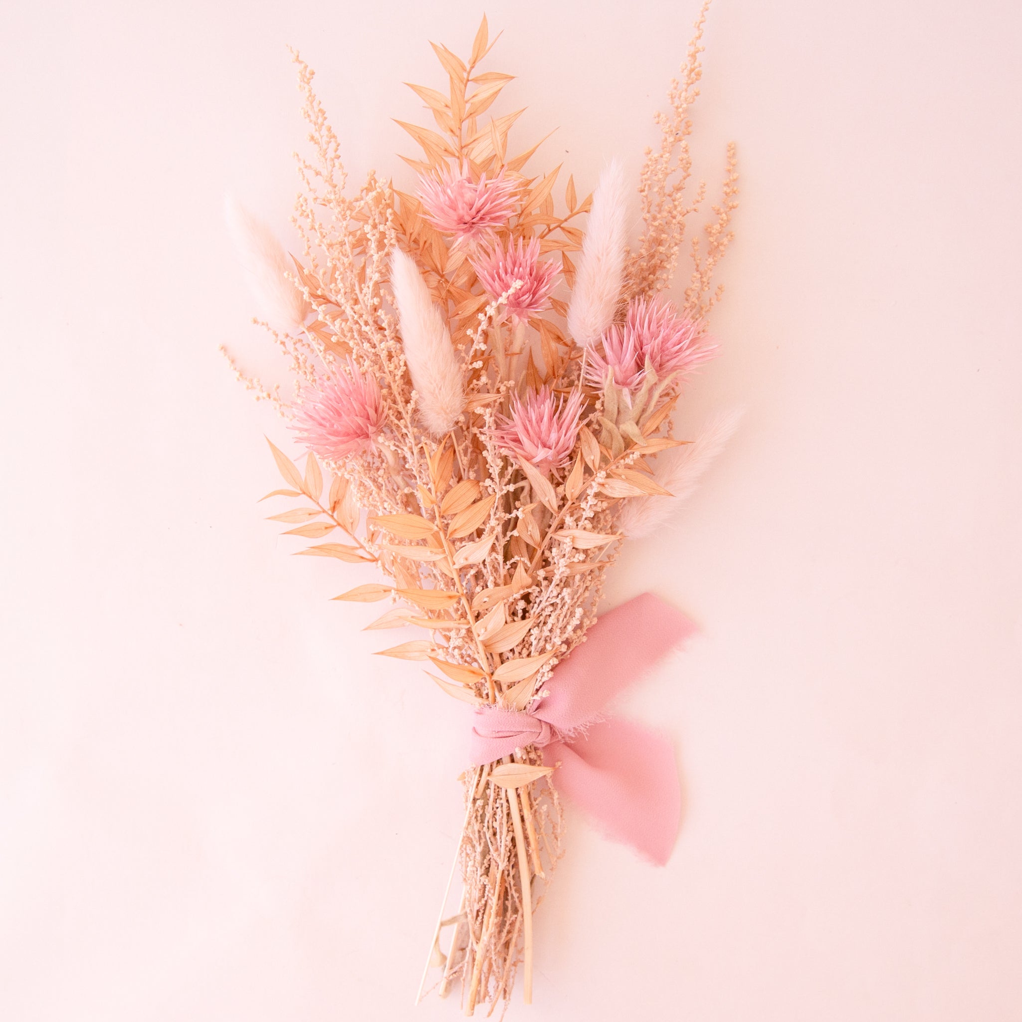 A bouquet of dried florals with tan and pink flowers tied with a pink bow. 