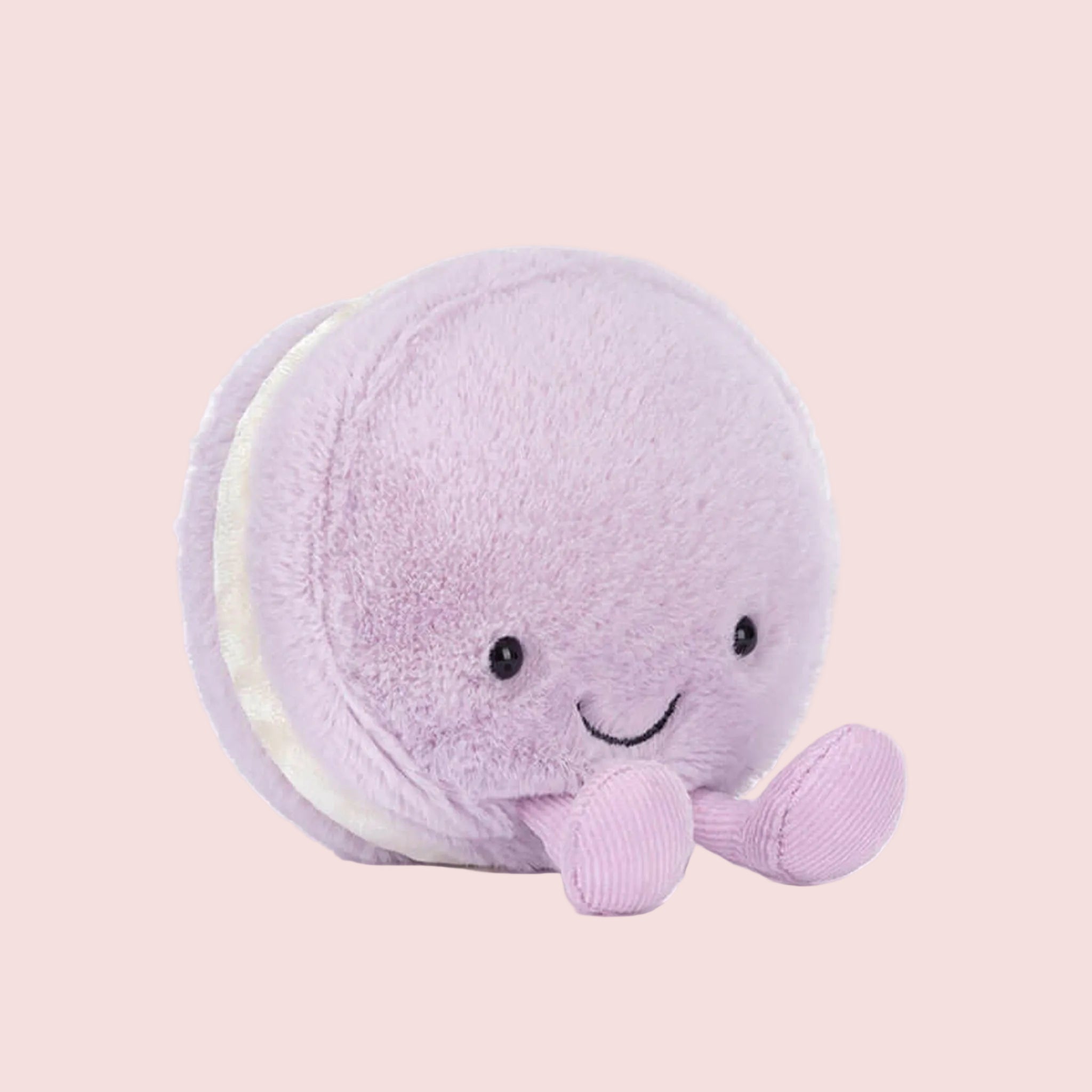 A macaron shaped stuffed toy with a smiling face and lavender corduroy legs and feet. 