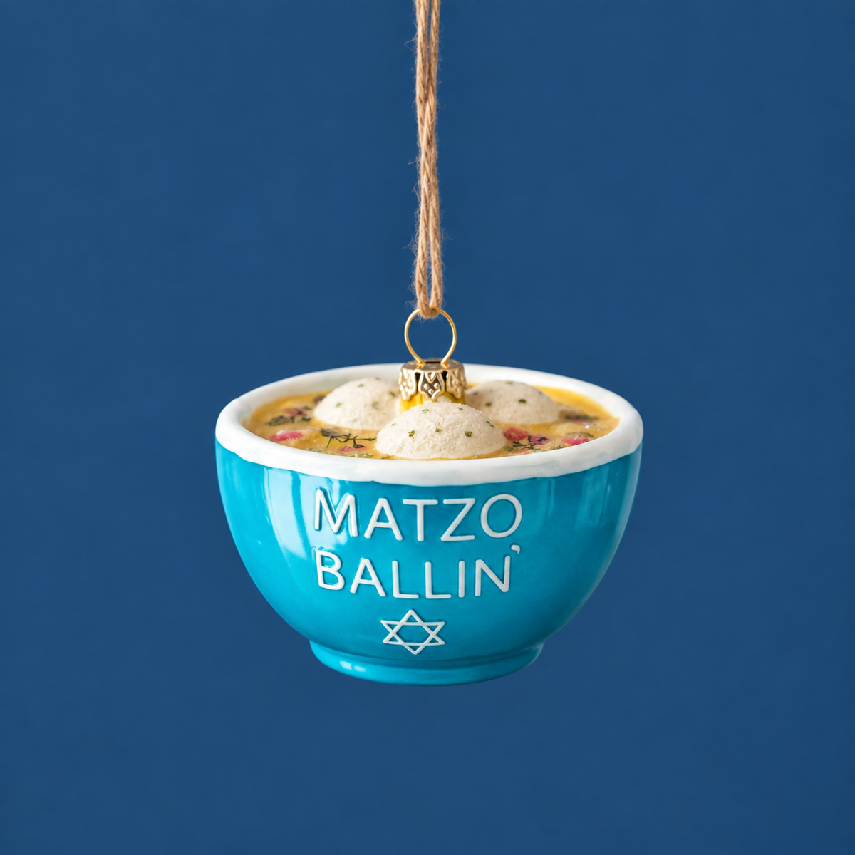A glass matzo ball soup ornament with dumplings and a blue bowl that says "matzo ballin" in white text.