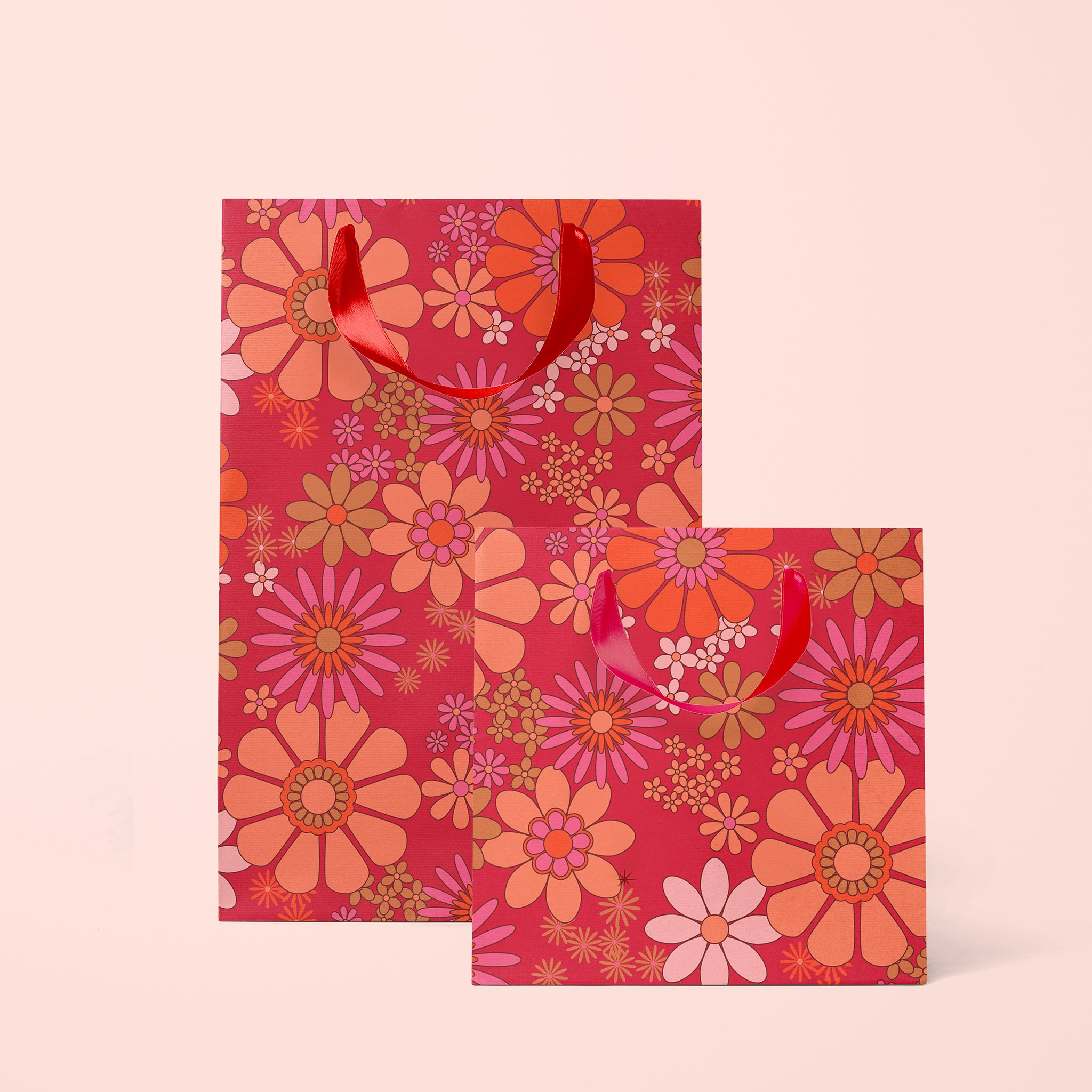 On a tan background is two gift bags with a pink, orange and hot pink floral print. 