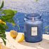 A blue decorative jarred candle with a lid and a rectangular white label in the center that reads, 'Mediterranean Lemon'. 