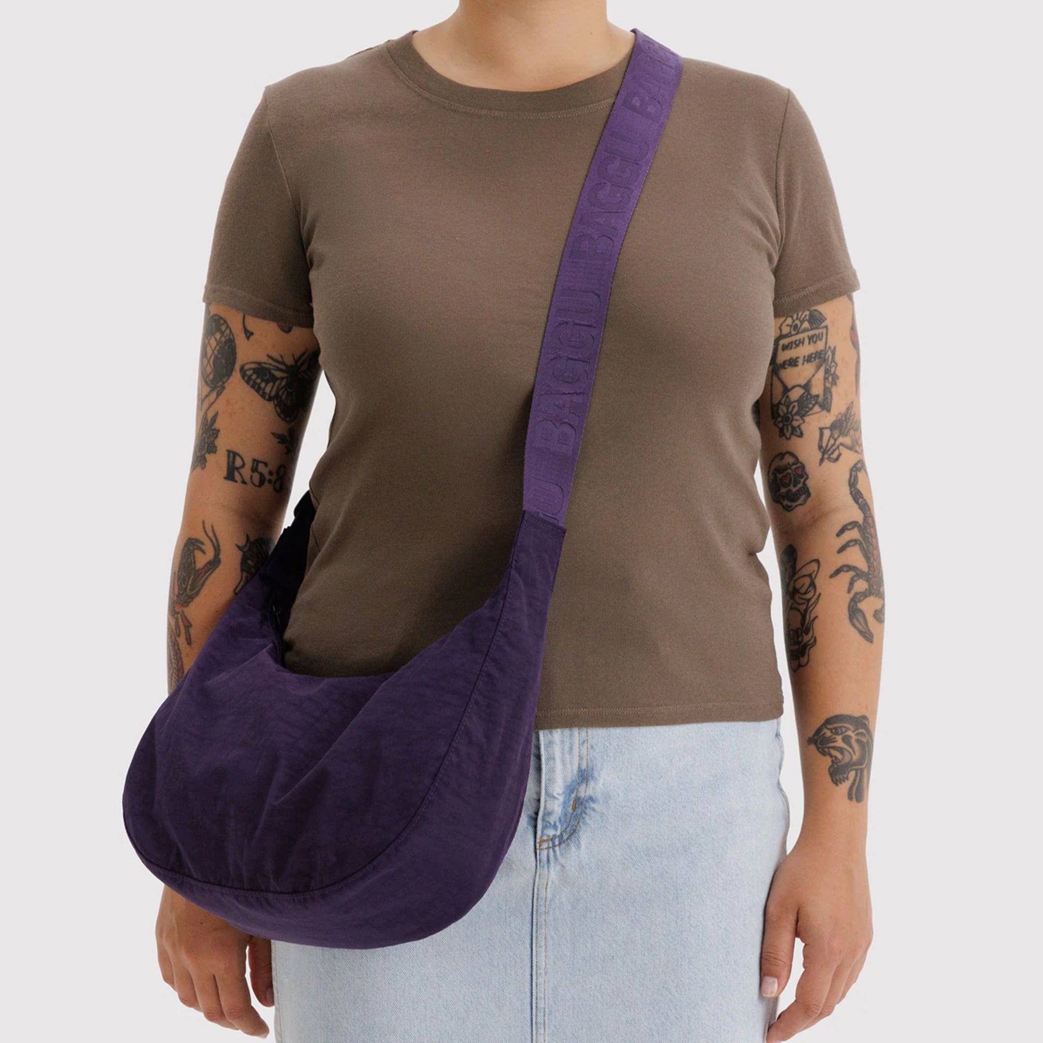 A dark purple crescent shaped nylon shoulder bag that can also be extended to a crossbody. 