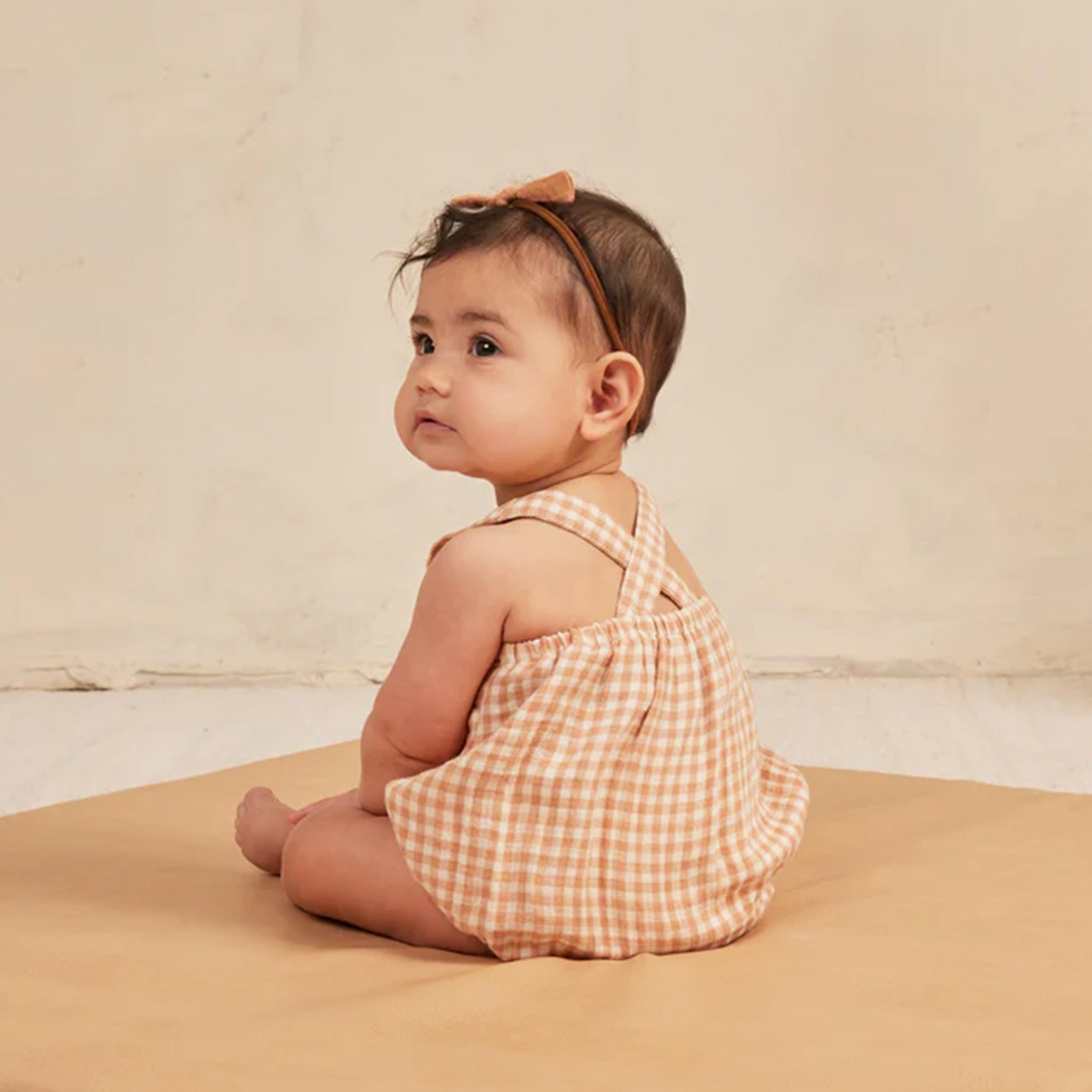 An ivory and light orange one piece children&#39;s romper with a criss cross detail on the back and snap closures on the bottom for easy changing. 