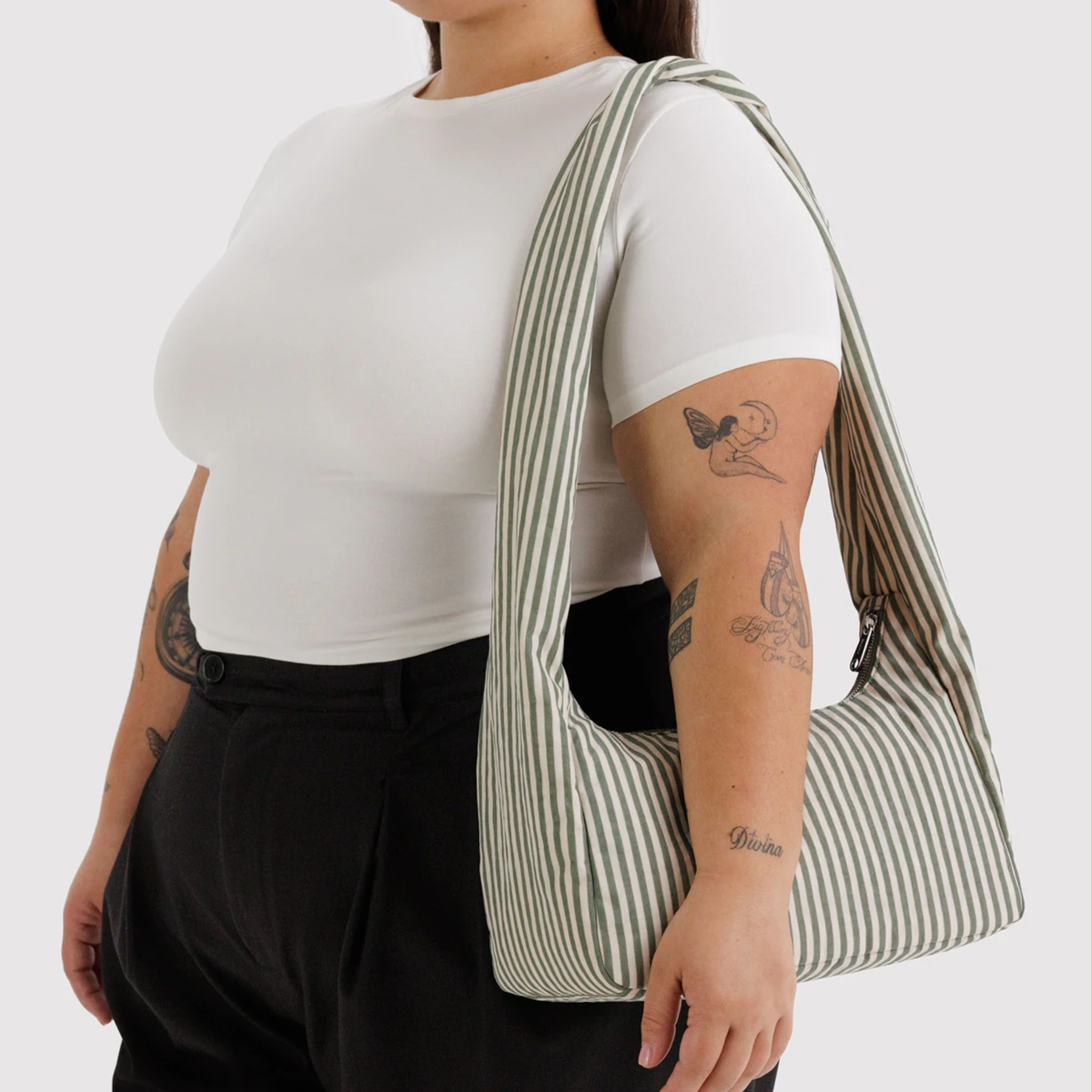 A sage striped nylon shoulder bag with long shoulder strap on a model's shoulder.