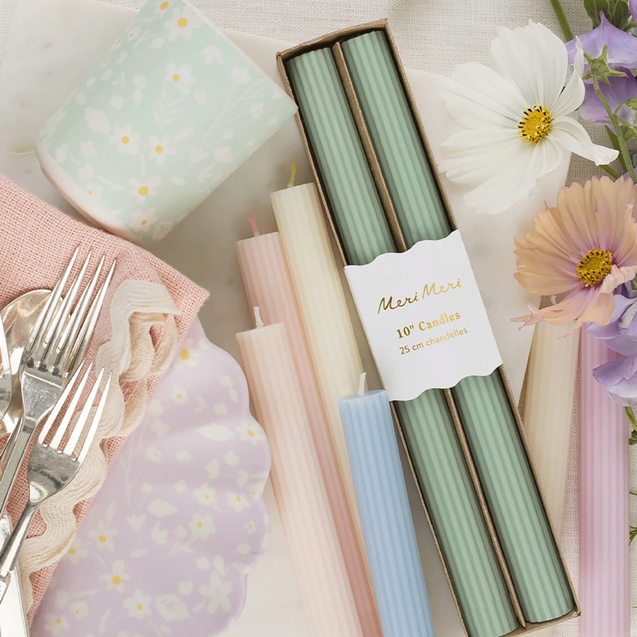 All the colors of the table candles photographed on a table next to pastel colored tableware and flowers. 
