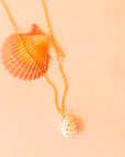A gold chain necklace with a white spotted shell pendant. 