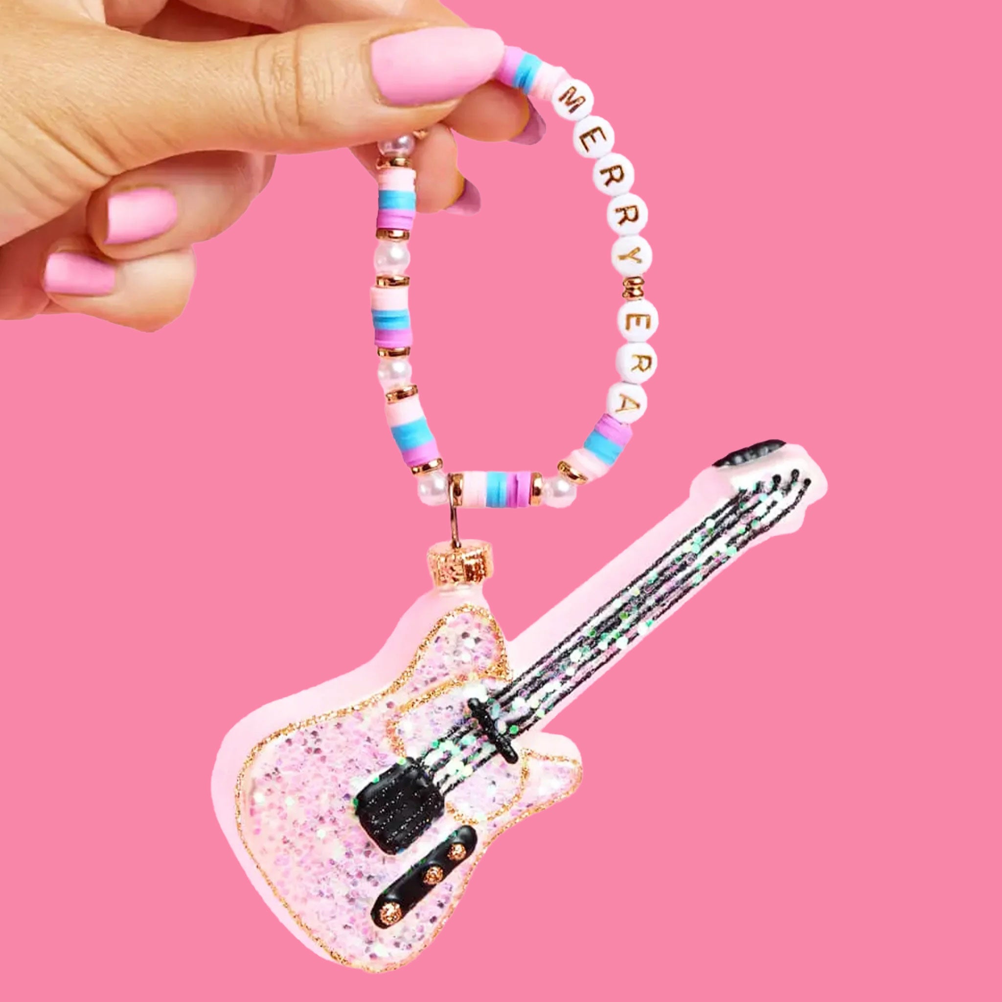 A pink glitter guitar ornament on a friendship bracelet hanger that reads "merry era"