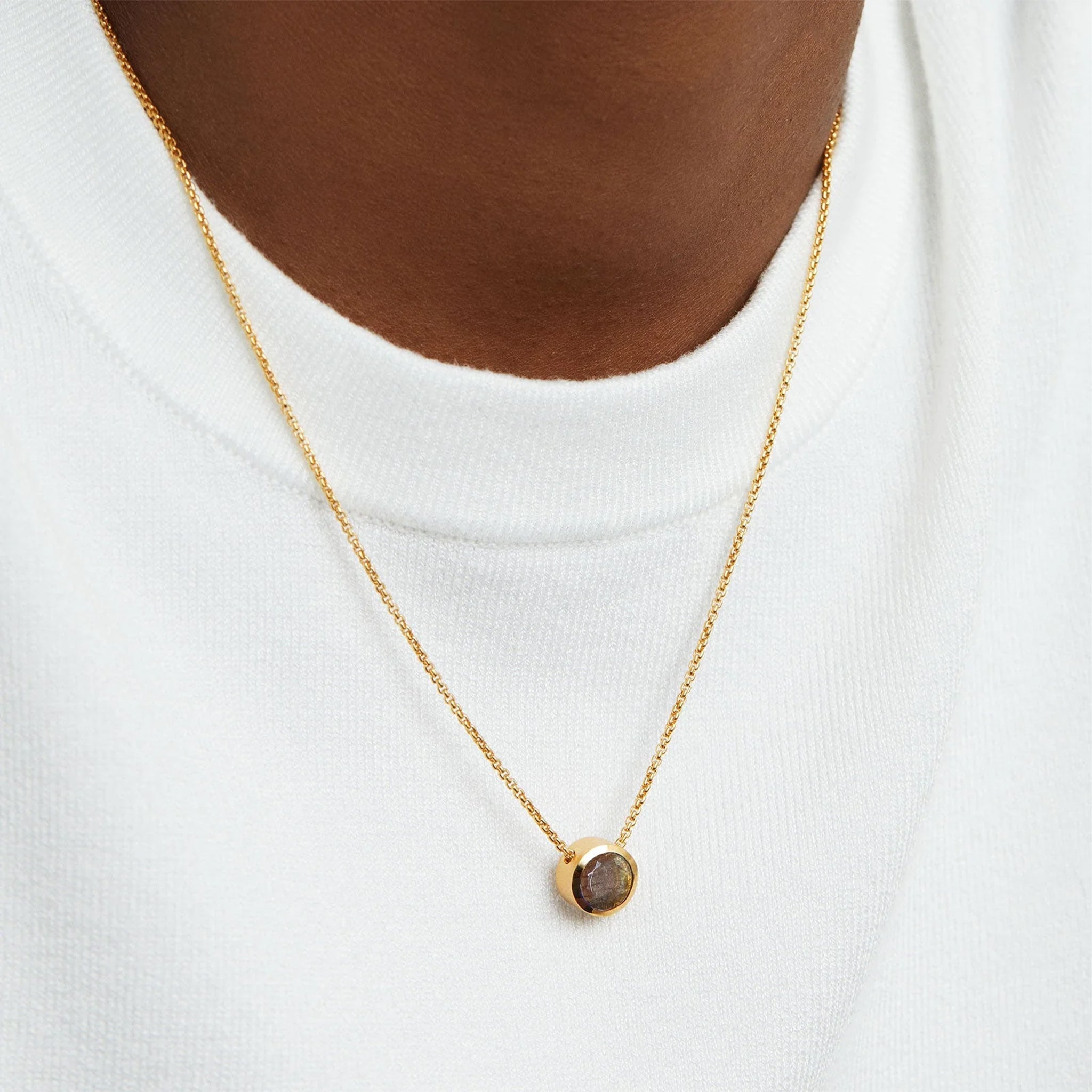 A gold chain necklace with a circle labradorite center. 