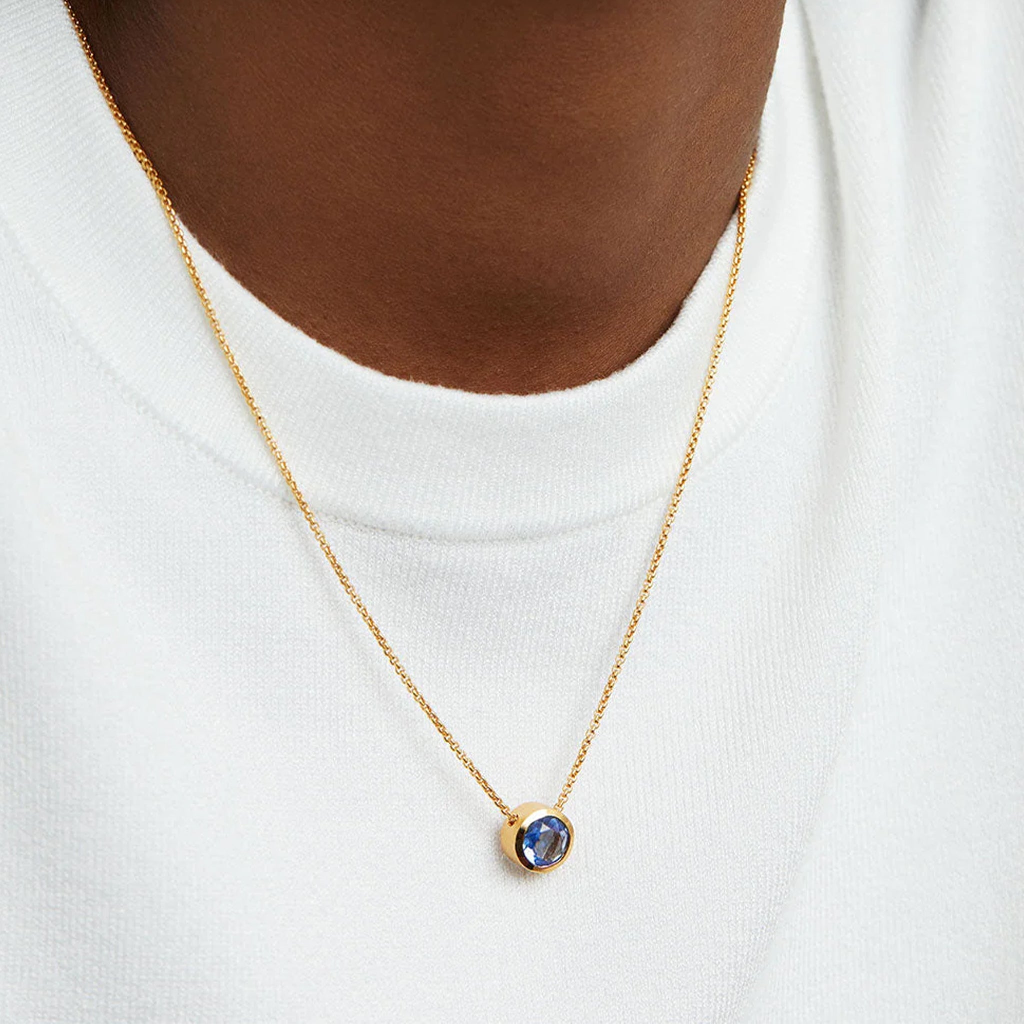 A gold chain necklace with a round midnight blue cz stone in the center. 
