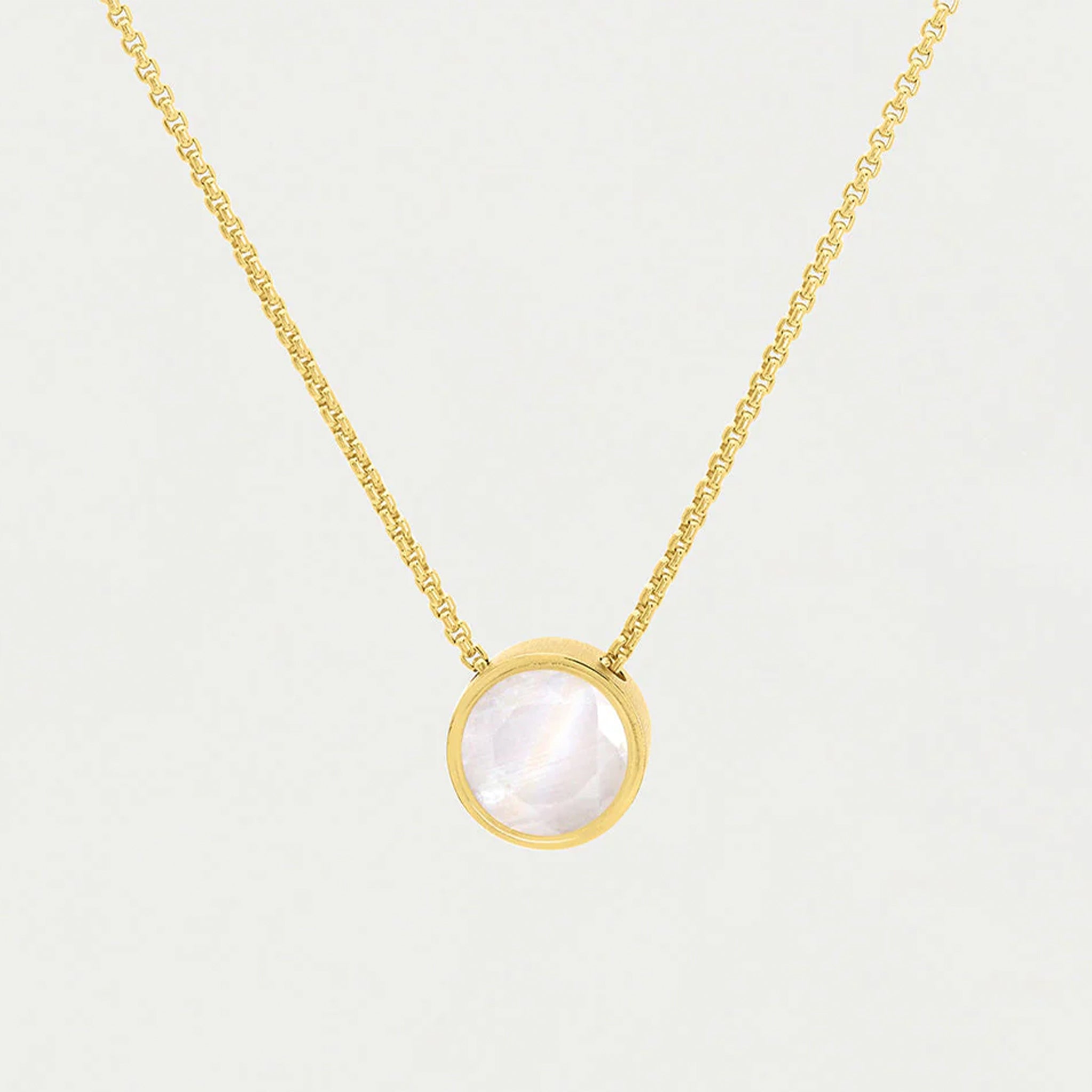 A gold chain necklace with a round pendant with a moonstone center. 