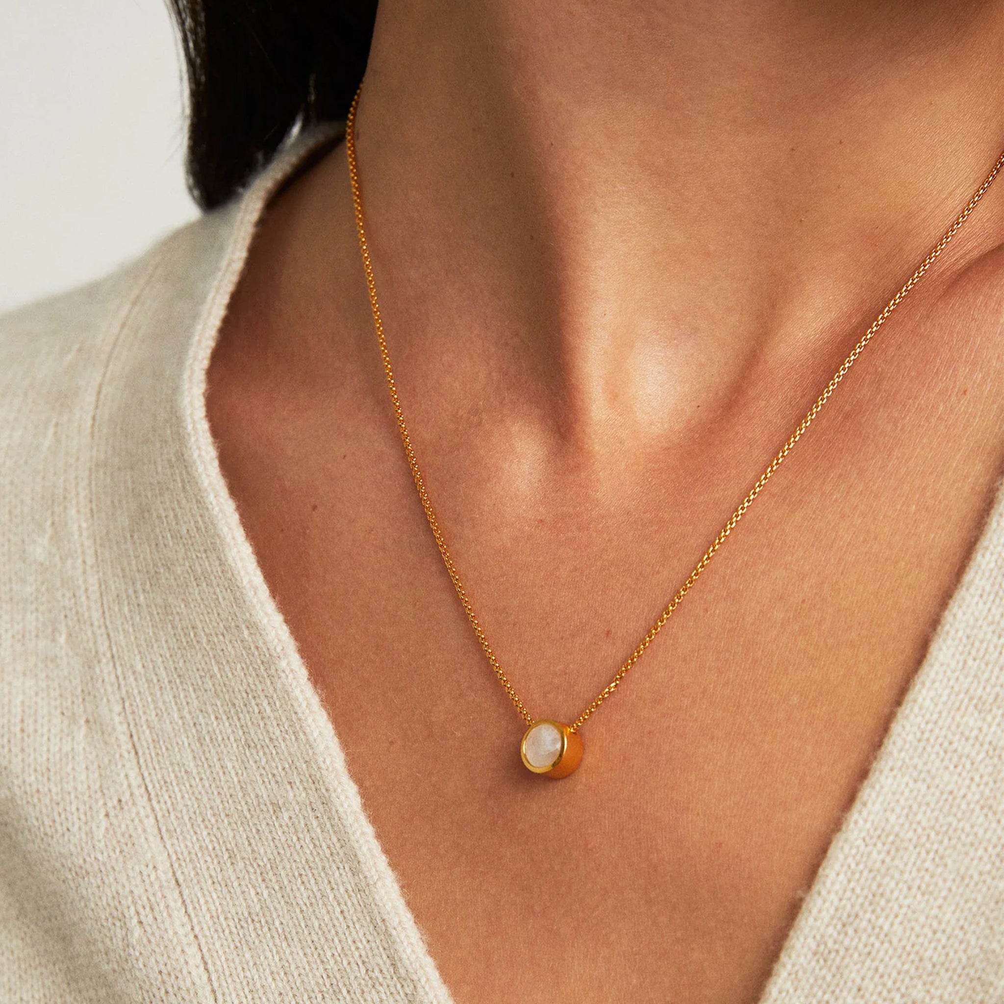 A gold chain necklace with a round pendant with a moonstone center. 