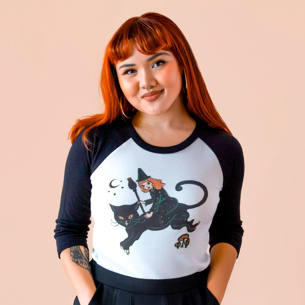 red headed model wearing a black and white tee shirt with a witch riding on a cat's back illustration.