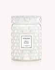 On a light pink background is a white glass jar candle with a milky effect to the glass along with a lid and a rectangular label in the center that reads, "Voluspa Milk Rose".