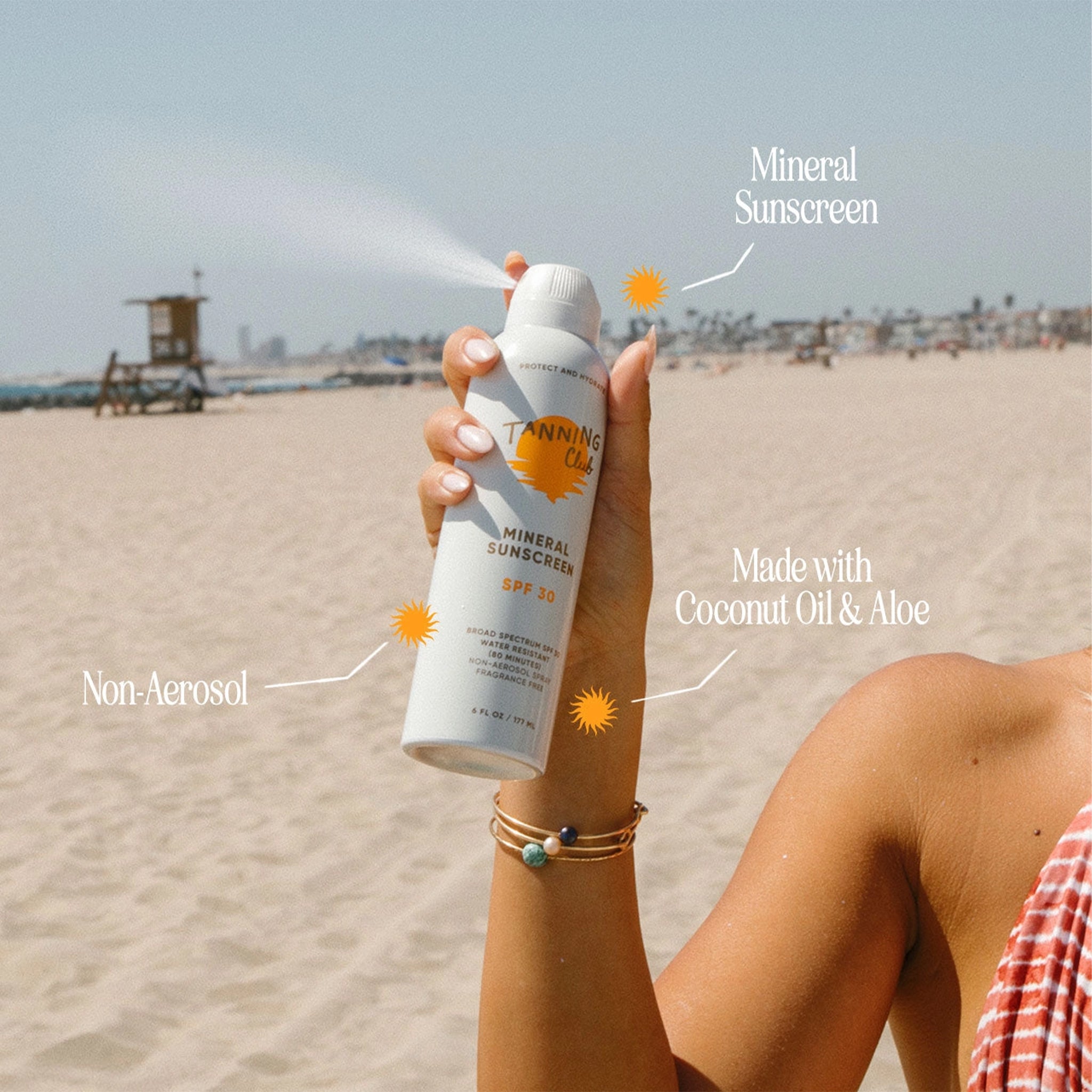 Person holding a can of Tanning Co. mineral sunscreen on a beach.