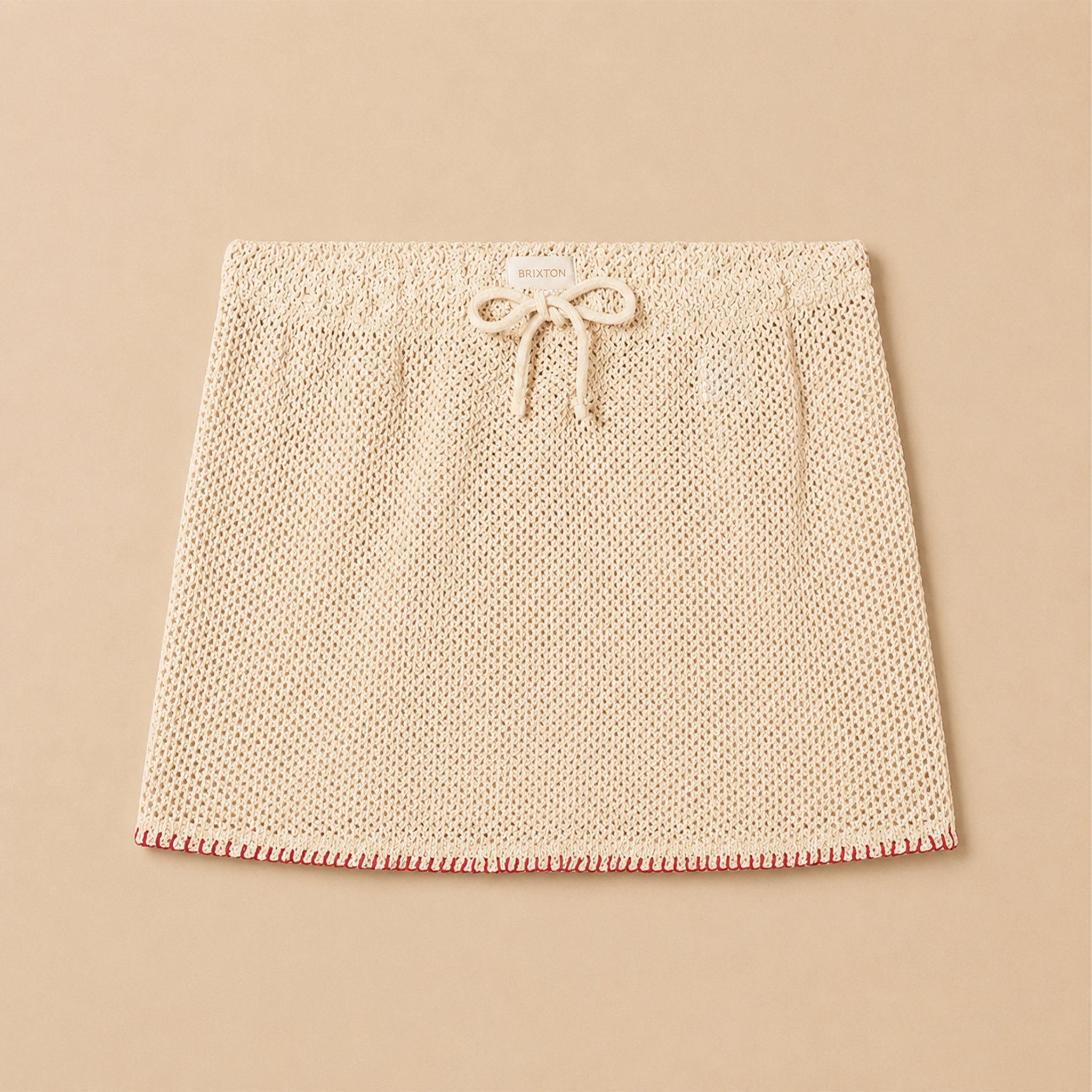 A tan crochet knit skirt with a red woven edge detail. 