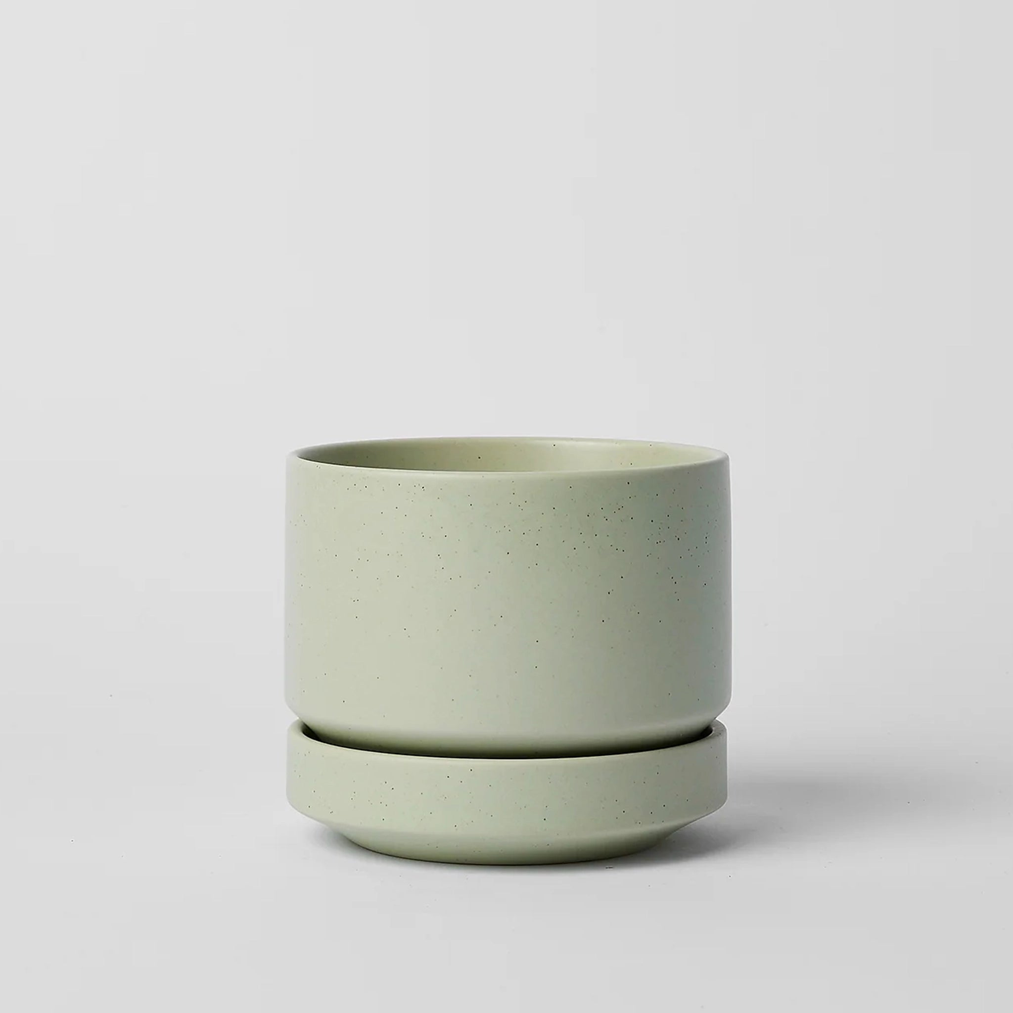 On a neutral background is a mint green speckled ceramic planter with a removable tray for watering. 