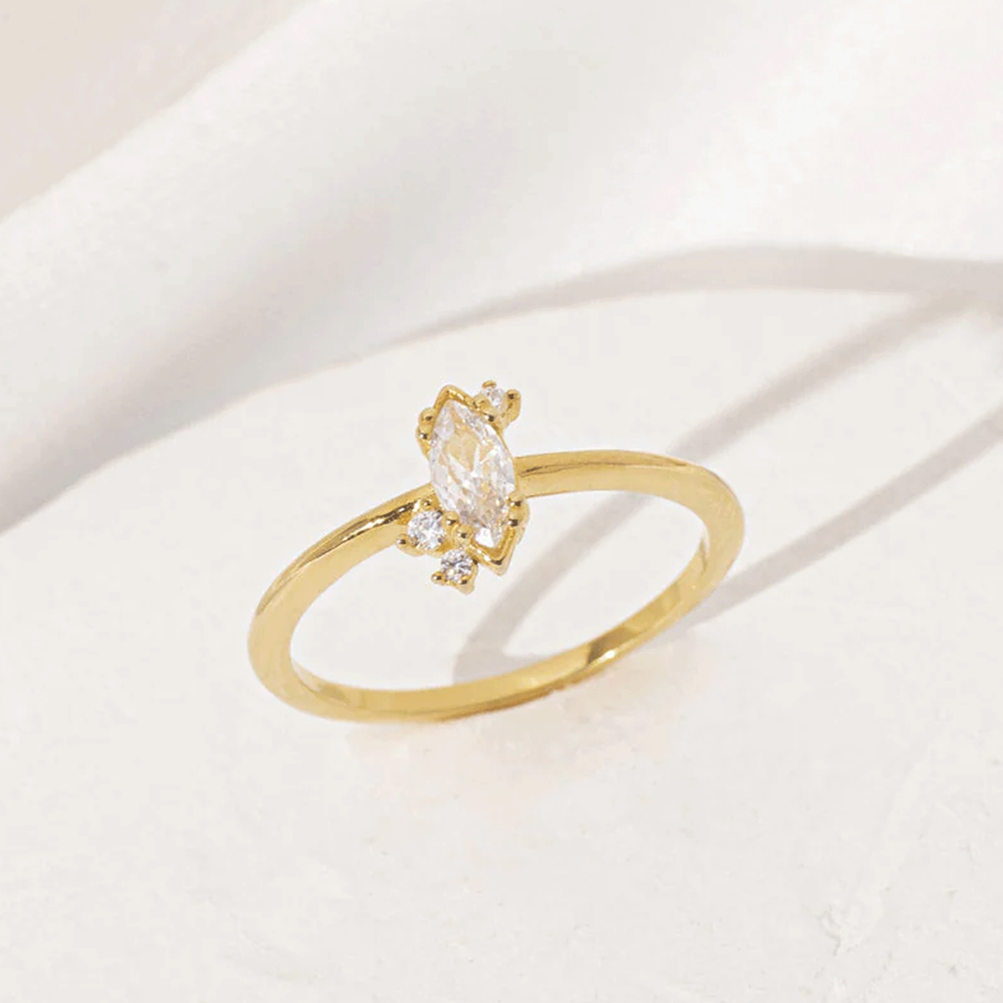 On a white background is a gold ring with a marquise shaped cubic zirconia with three smaller stones, two towards the bottom and on the top. 