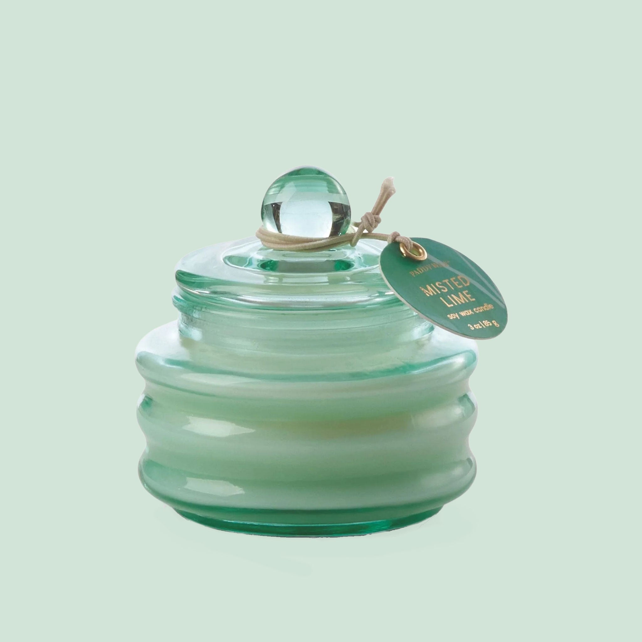 A seaglass colored glass candle sits in the middle of page with a tag that reads "misted lime"