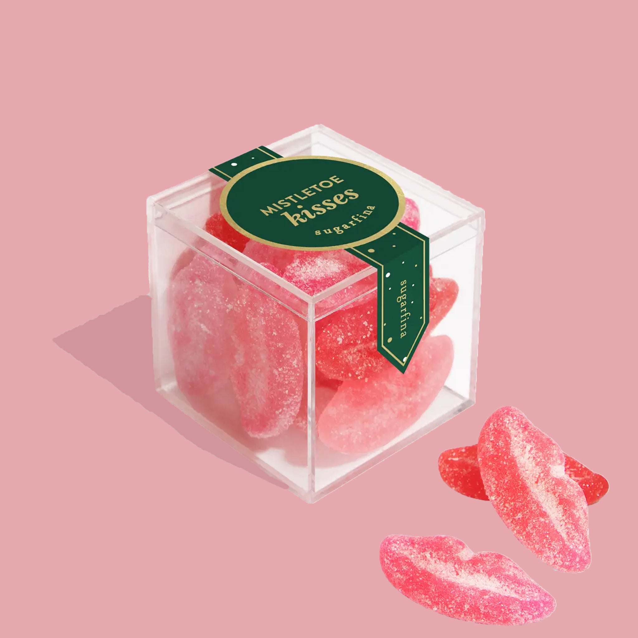 A clear acrylic box of pink lip shaped gummy candies with text on the label that reads, 'Mistletoe Kisses sugarfina". 