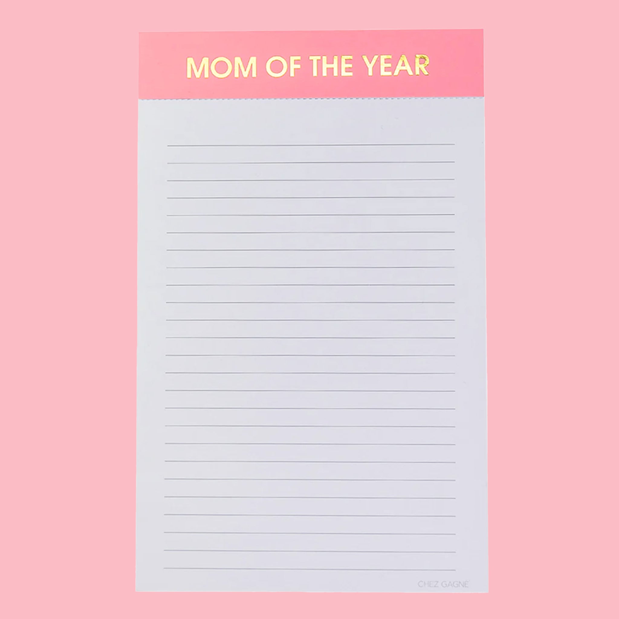 On a pink background is a lined notepad with a pink header that reads, &quot;MOM OF THE YEAR&quot; in gold foil letters. 