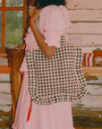 A black and white gingham print tote bag with ruffle details and shoulder straps. 