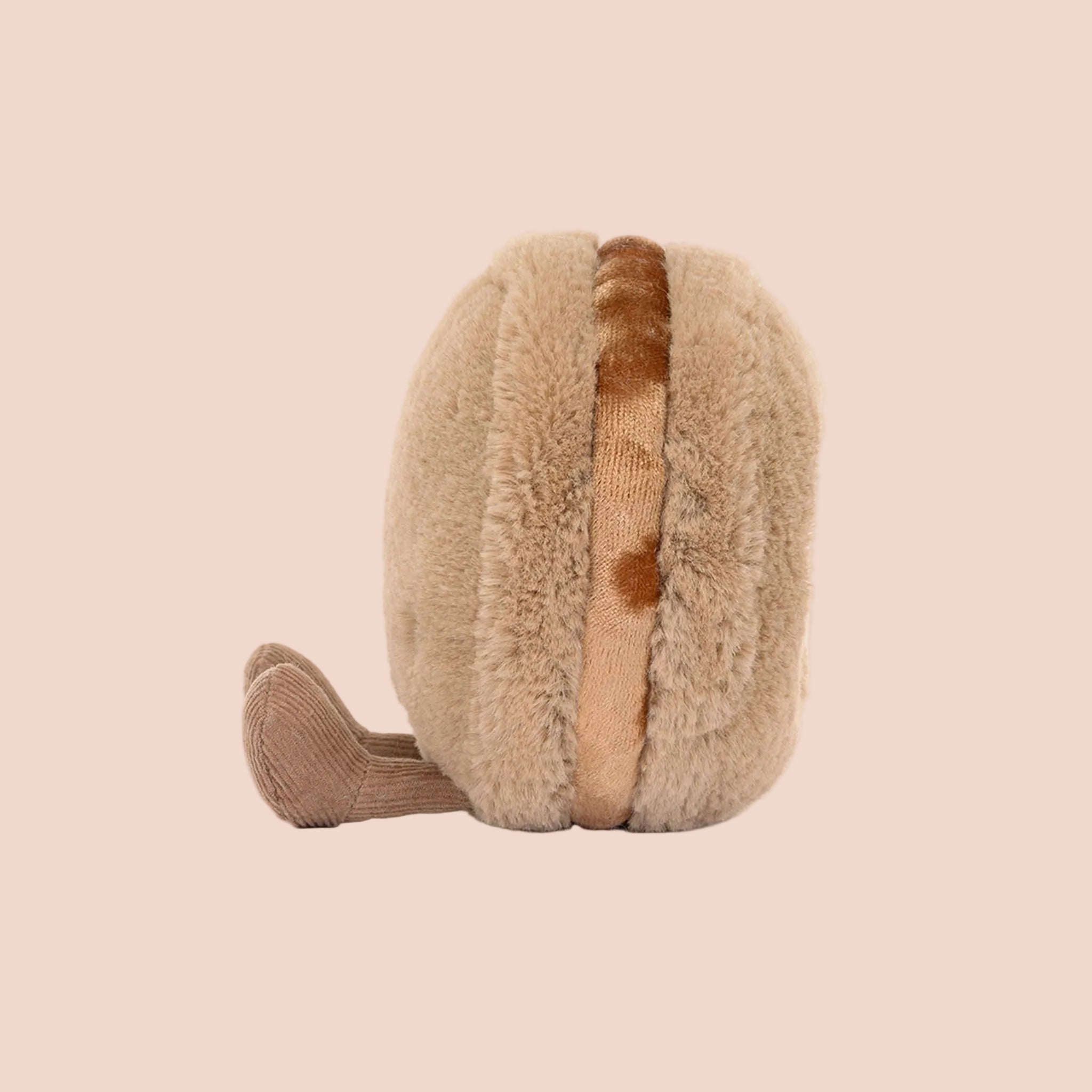 A brown macaron shaped stuffed toy with a smiling face and brown corduroy legs and feet. 