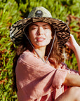 A black and ivory monster printed straw hat with a drawstring knot neck strap. 