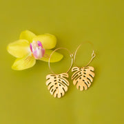 A thin gold hoop with a outlined gold monstera leaf charm hanging from the hoop.