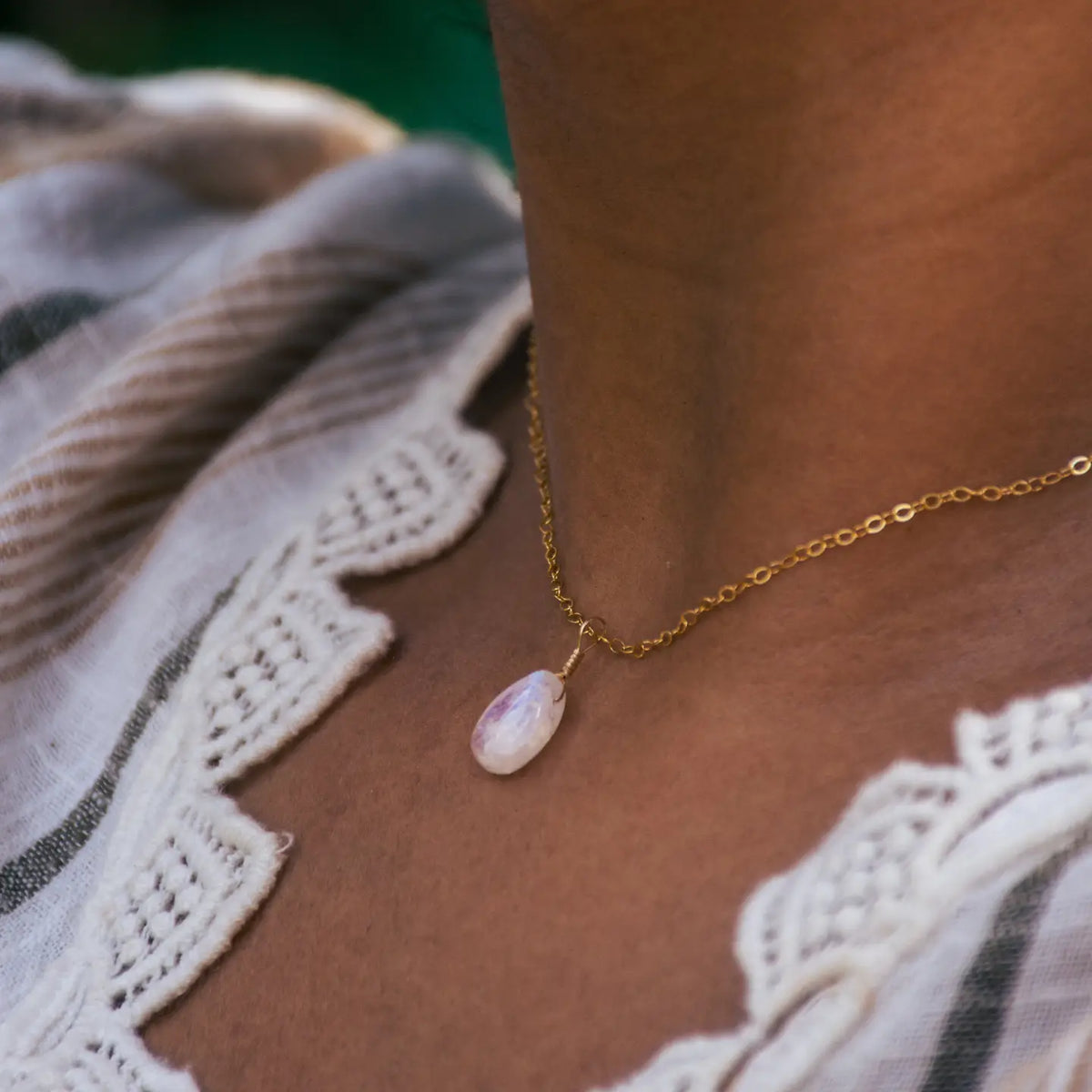 A moonstone teardrop shaped necklace on a gold chain worn on a model's neck.