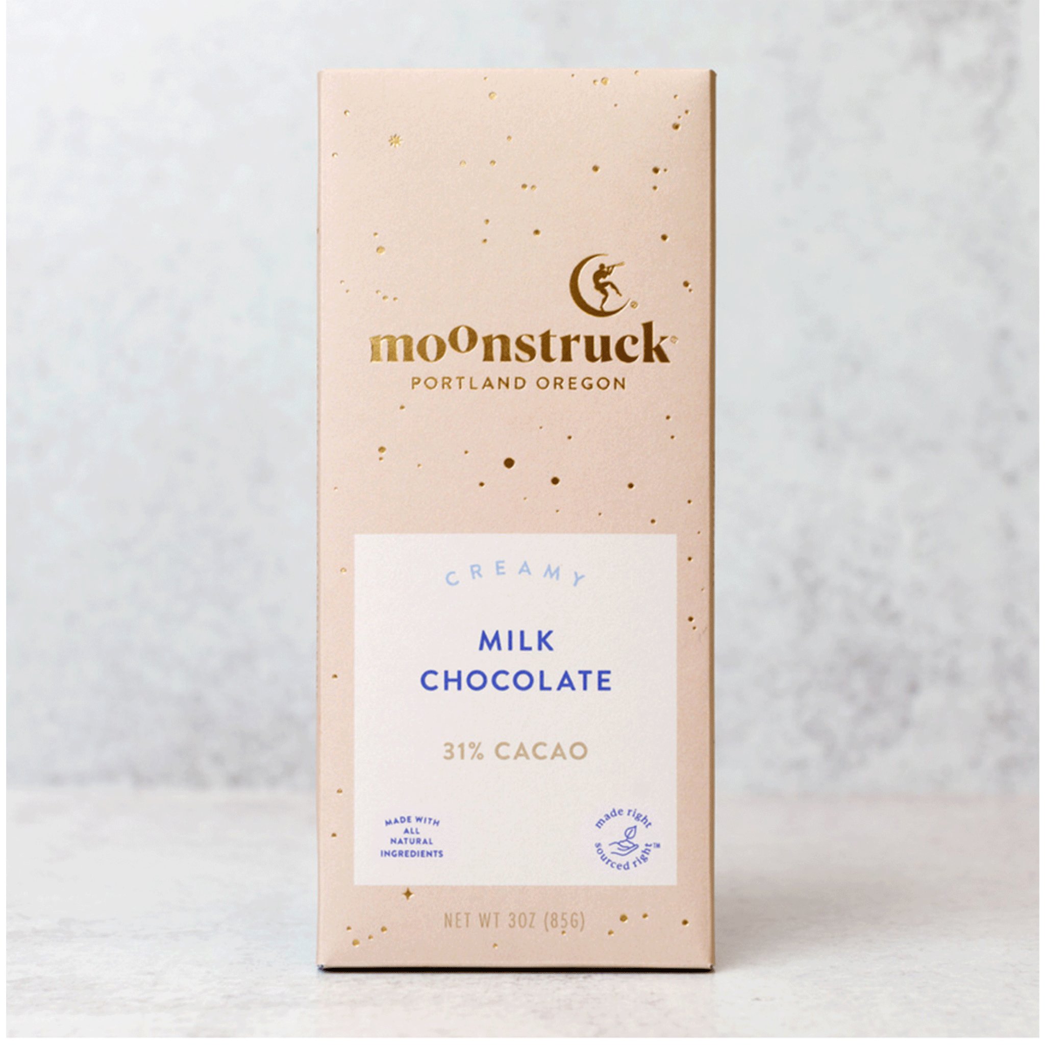 On a grey background is a tan packaged chocolate bar with gold details and text that reads, "moonstruck Portland Oregon", "Creamy Milk Chocolate 31% Cacao".