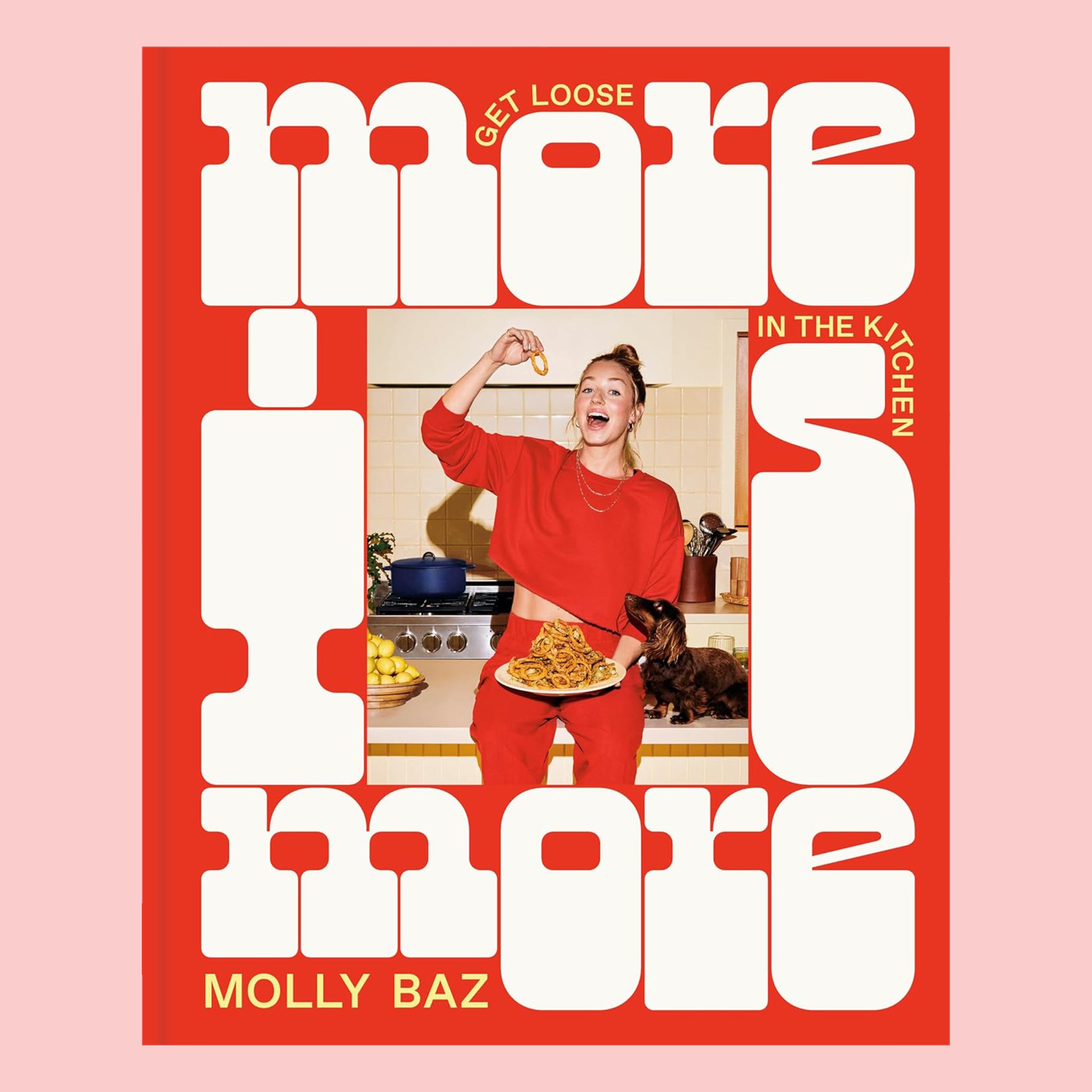 On a pink background is a red and white book cover with a photo of a person in red with a plate full of food and white text around that reads, "more is more". 