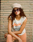 Model is wearing a white tank top, and is styled with a beige hat and black sunglasses. 