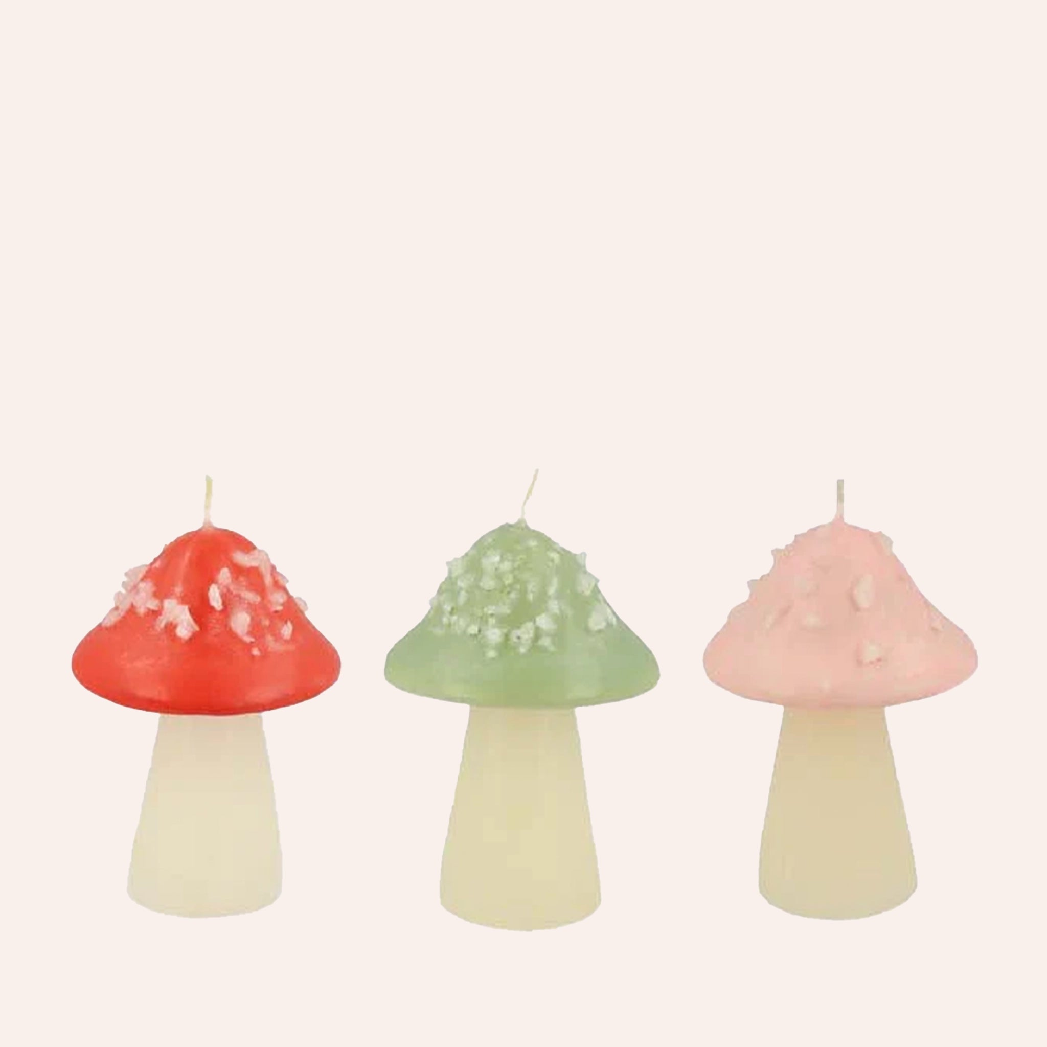 On a light pink background is a set of three mushroom shaped candles in three different colors, red, green and pink. 