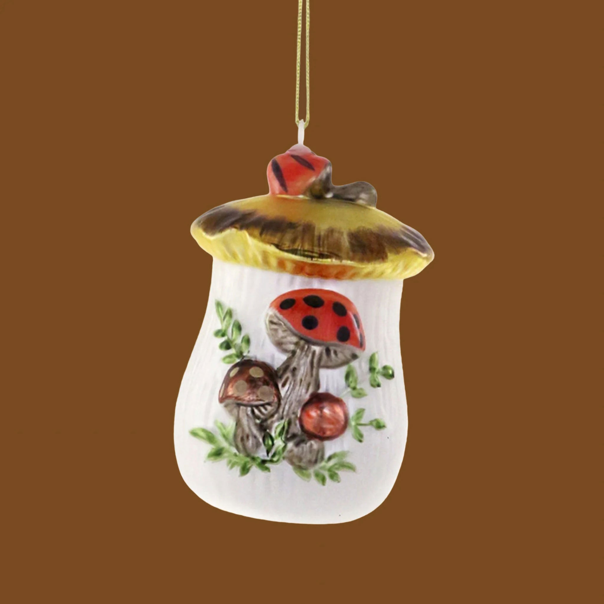 On a green background is an ivory and red glass ornament in the shape of a cookie jar with a mushroom design on it.