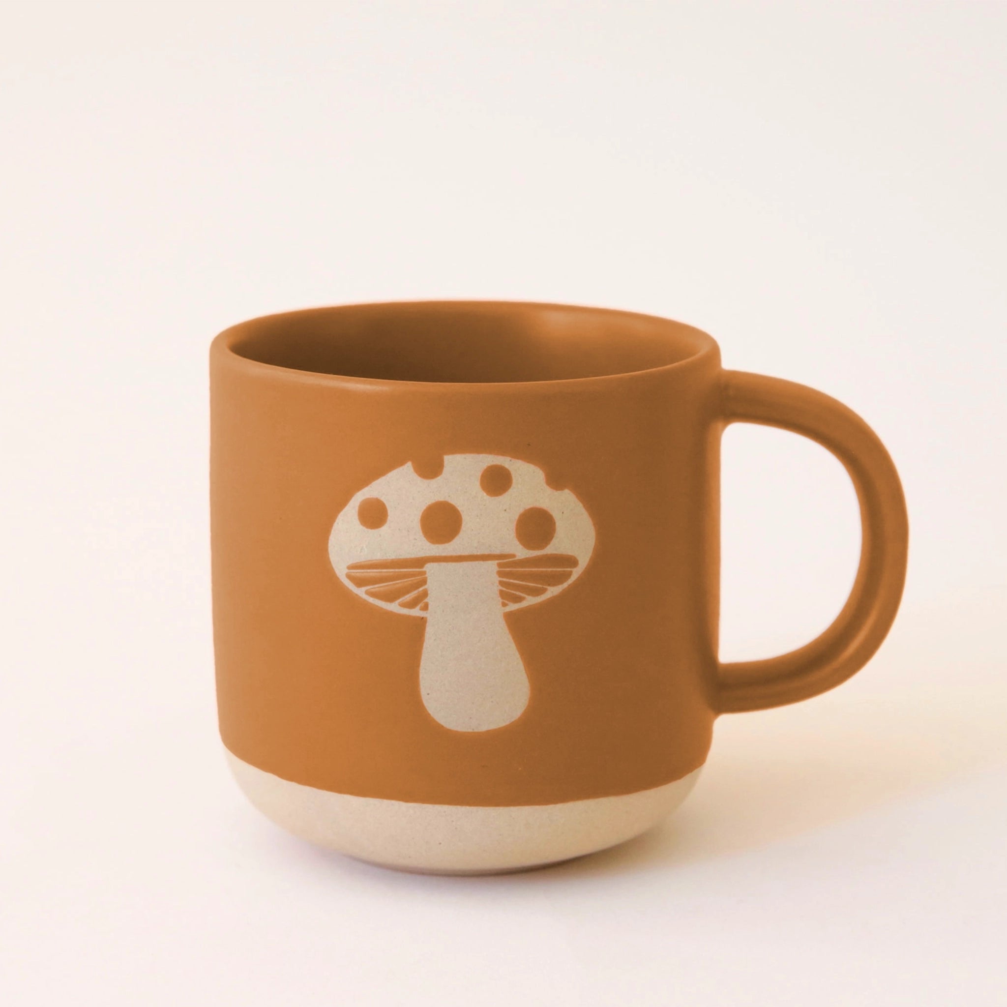 A ceramic mug with a warm brown tone with a mushroom design in the center. 