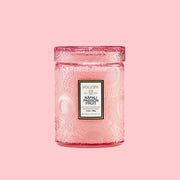 A small pink decorative jar candle with a rectangular label that reads, "Voluspa Napali Passion Fruit". 