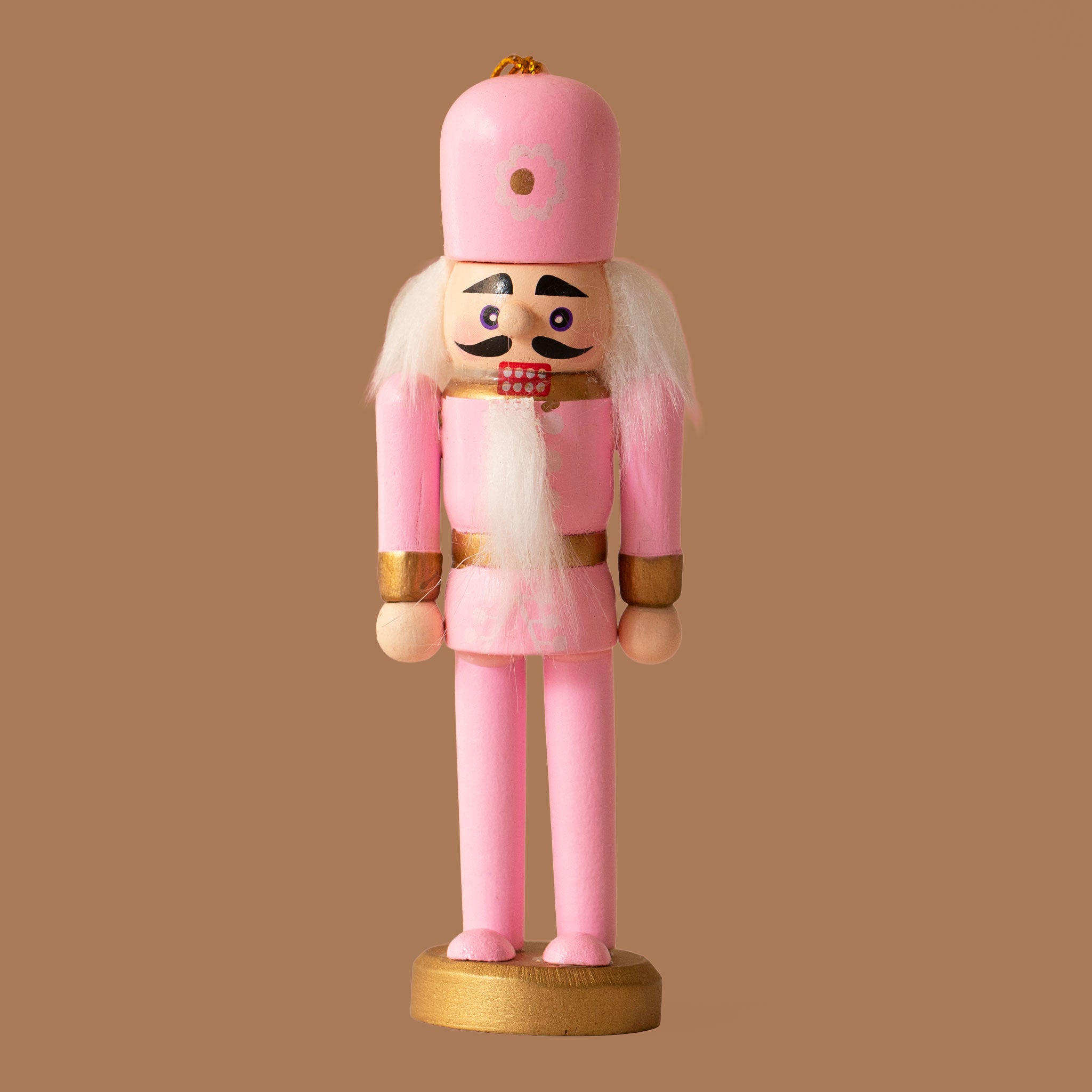 A pink wooden nutcracker figure with a tall pink hat, white hair and beard, gold accents, and a gold round base, standing against a warm brown background.